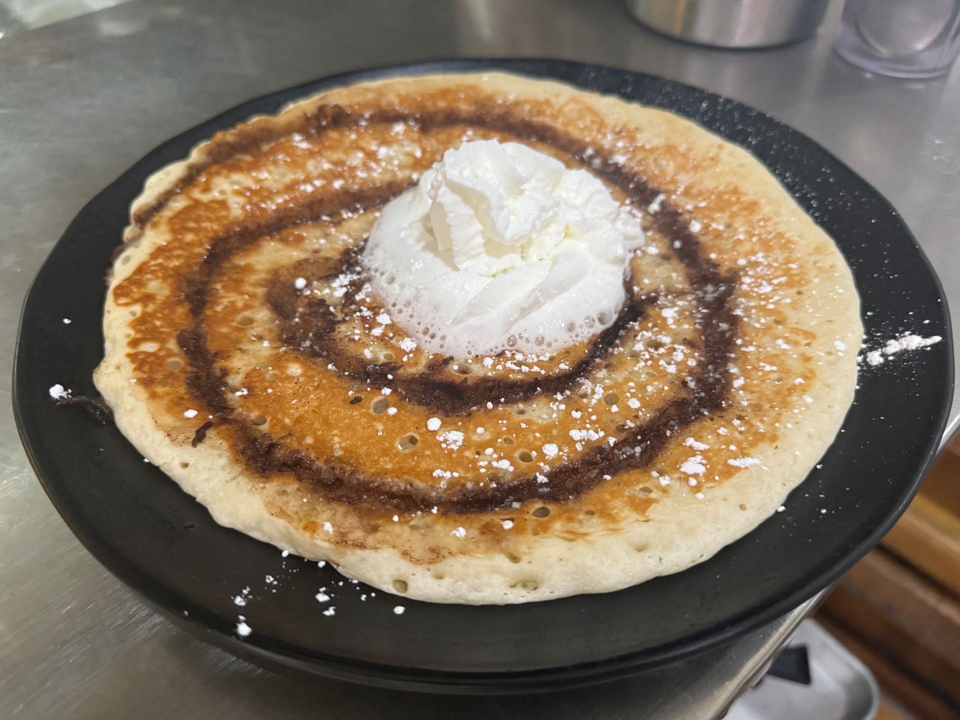 A pancake with whipped cream on top is on a black plate.