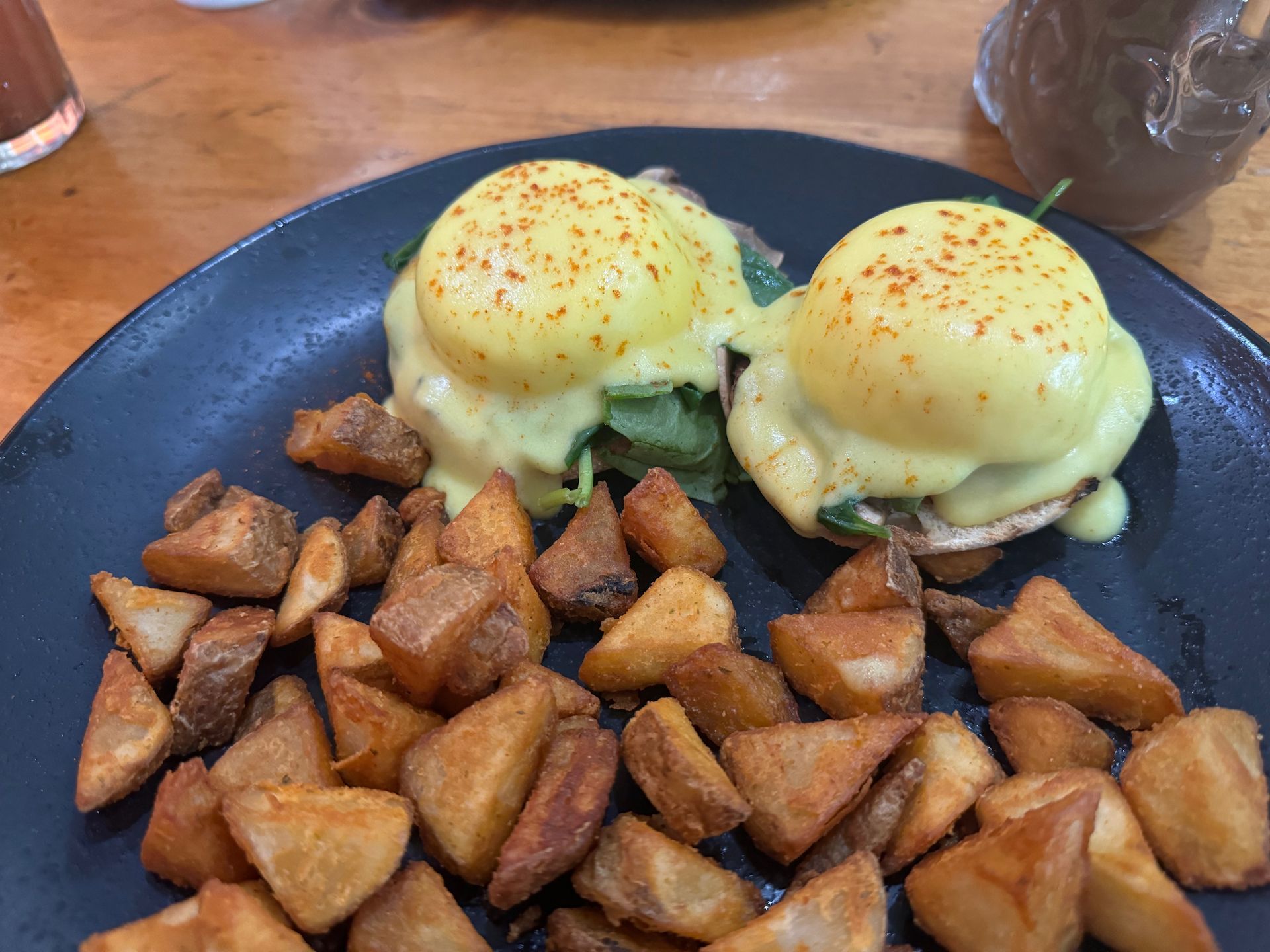 A black plate topped with eggs benedict and potatoes on a table.