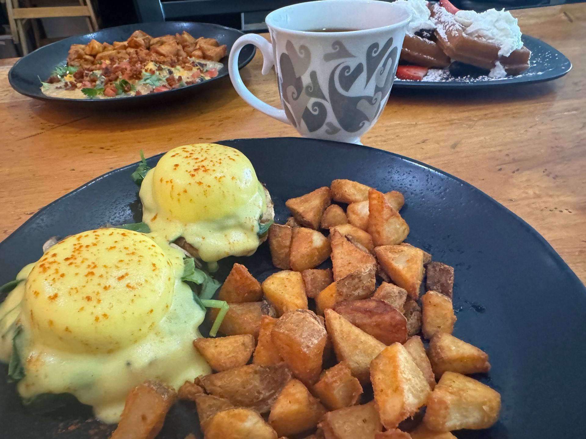 A plate of food with potatoes and eggs on a table next to a cup of coffee.