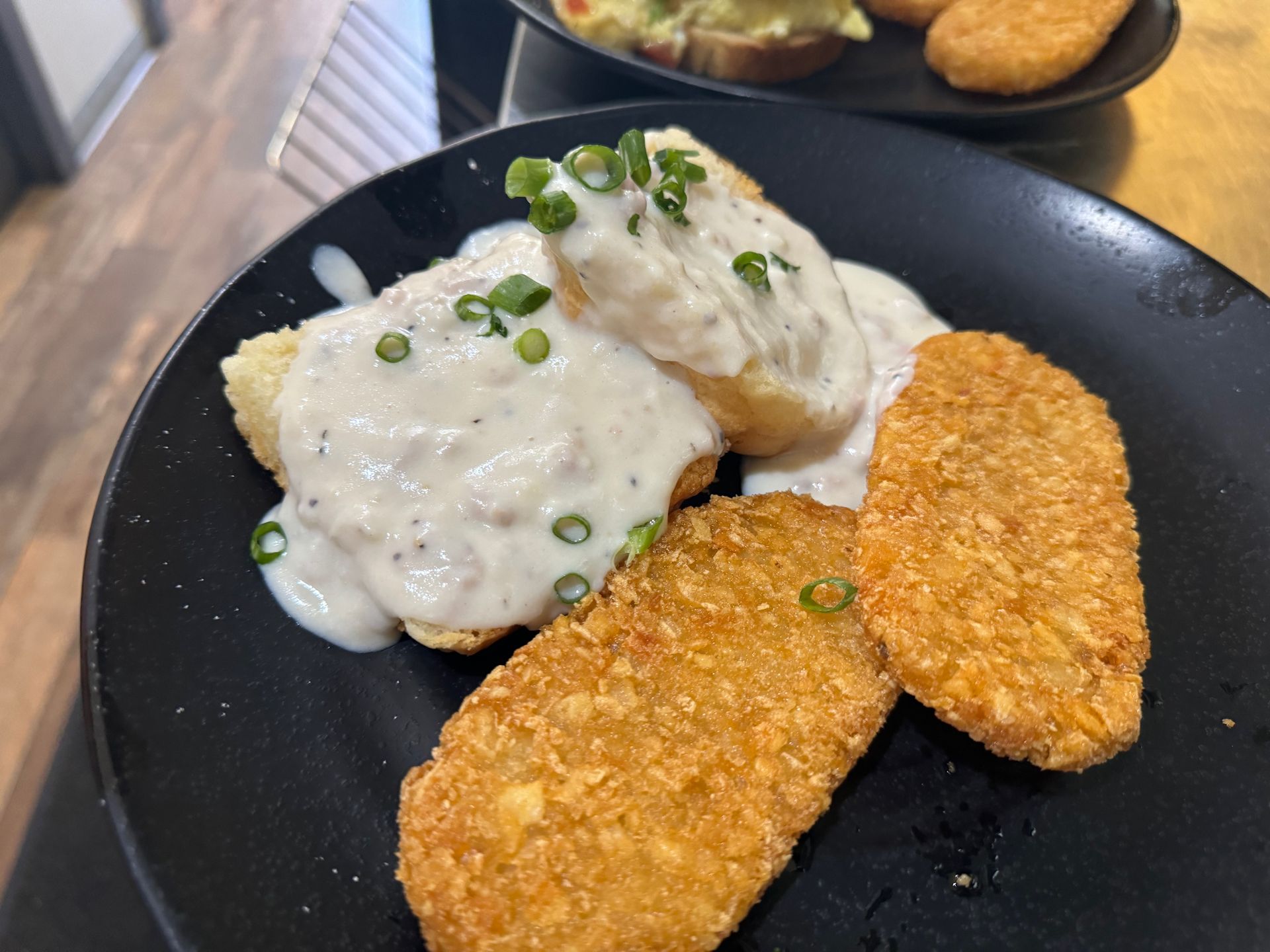 A black plate topped with biscuits and gravy and hash browns