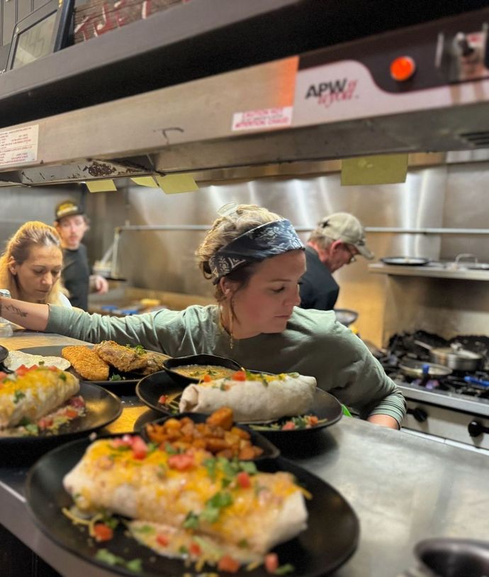 A woman in a kitchen with plates of food and a sign that says apw