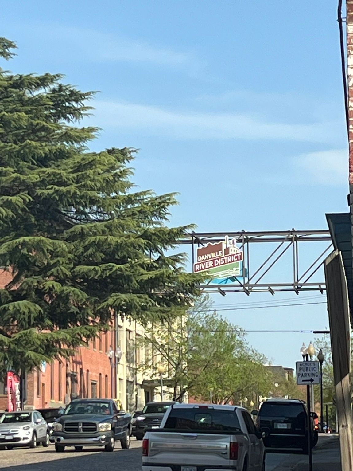 Street scene with cars, buildings, trees, and a sign under a blue sky.