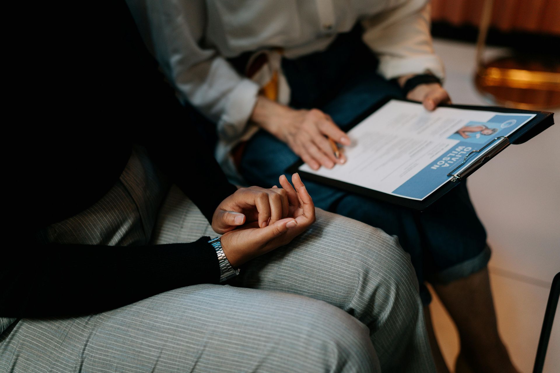 Person reviewing a document in a light blue binder, seated with another person.