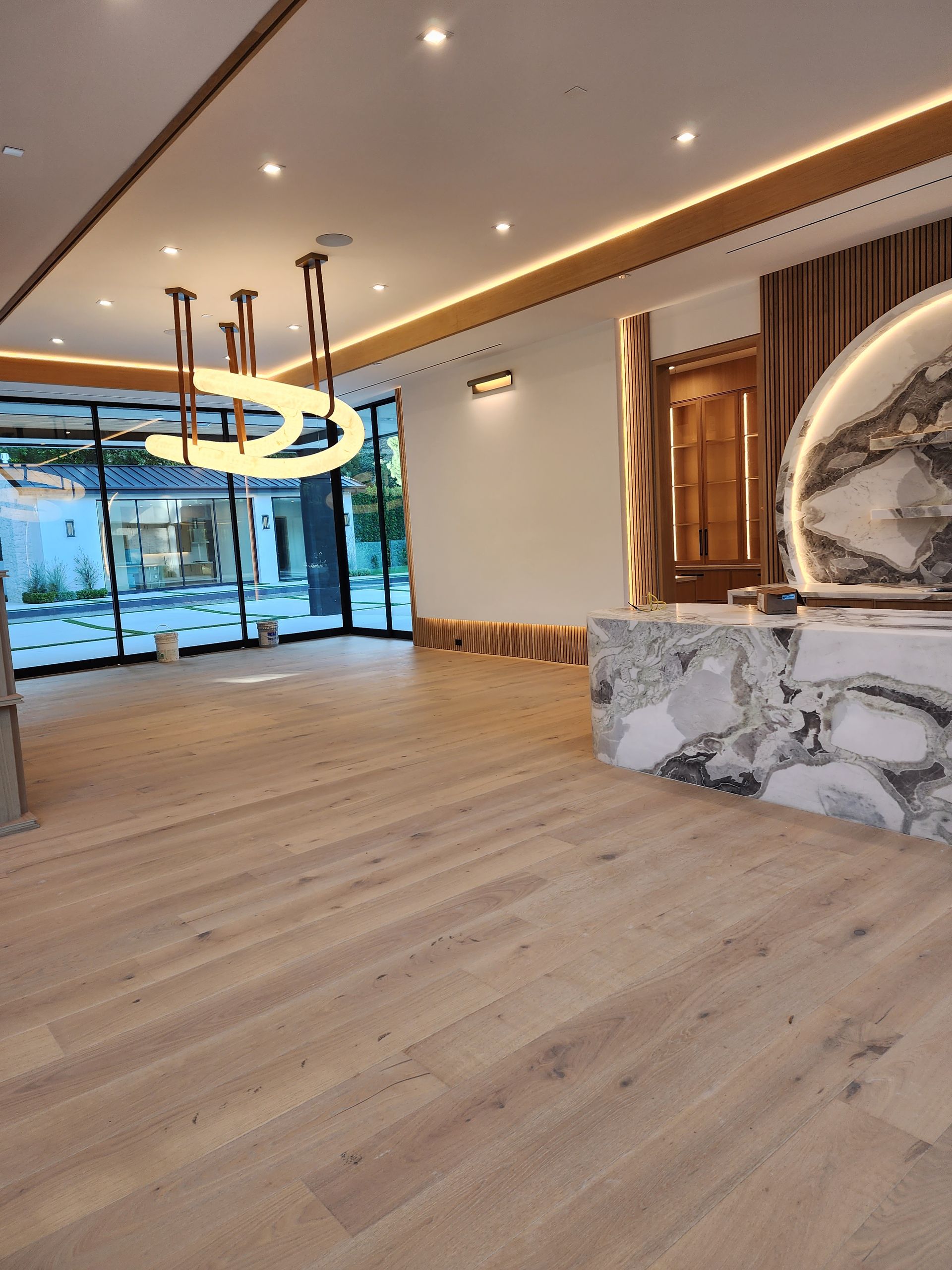 Spacious interior with wood flooring, large windows, marble counter, and modern lighting fixtures.