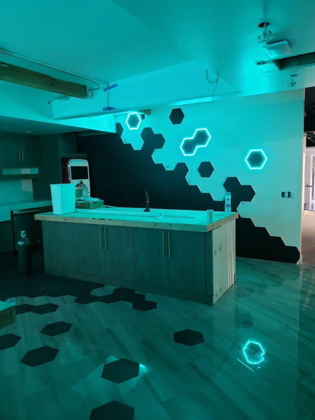 A room with turquoise lighting, a wooden countertop, a black hexagon wall, and hexagon accents on the floor and wall.
