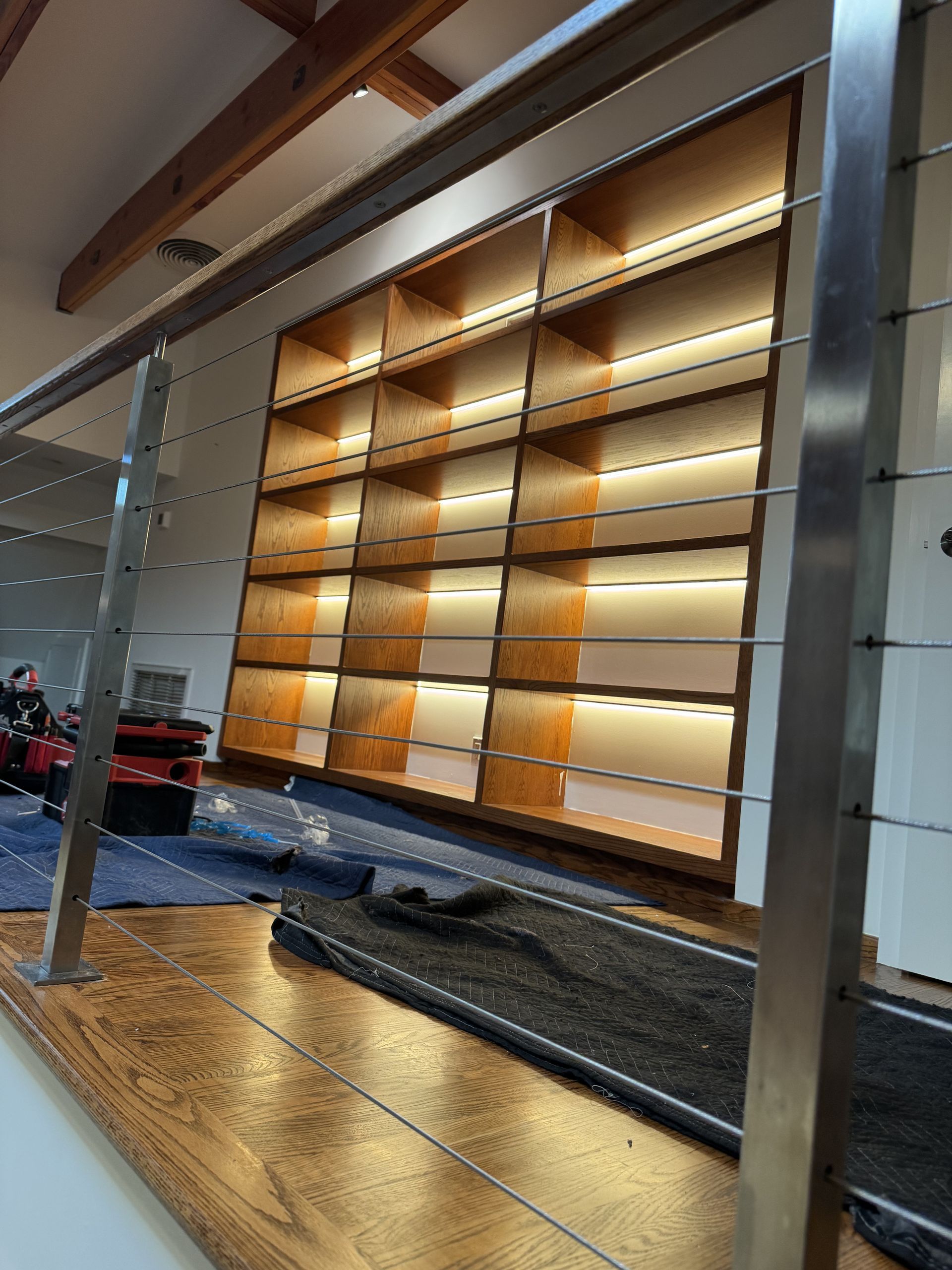 Wooden shelving unit with backlighting, viewed from above, with a stainless steel railing in the foreground.