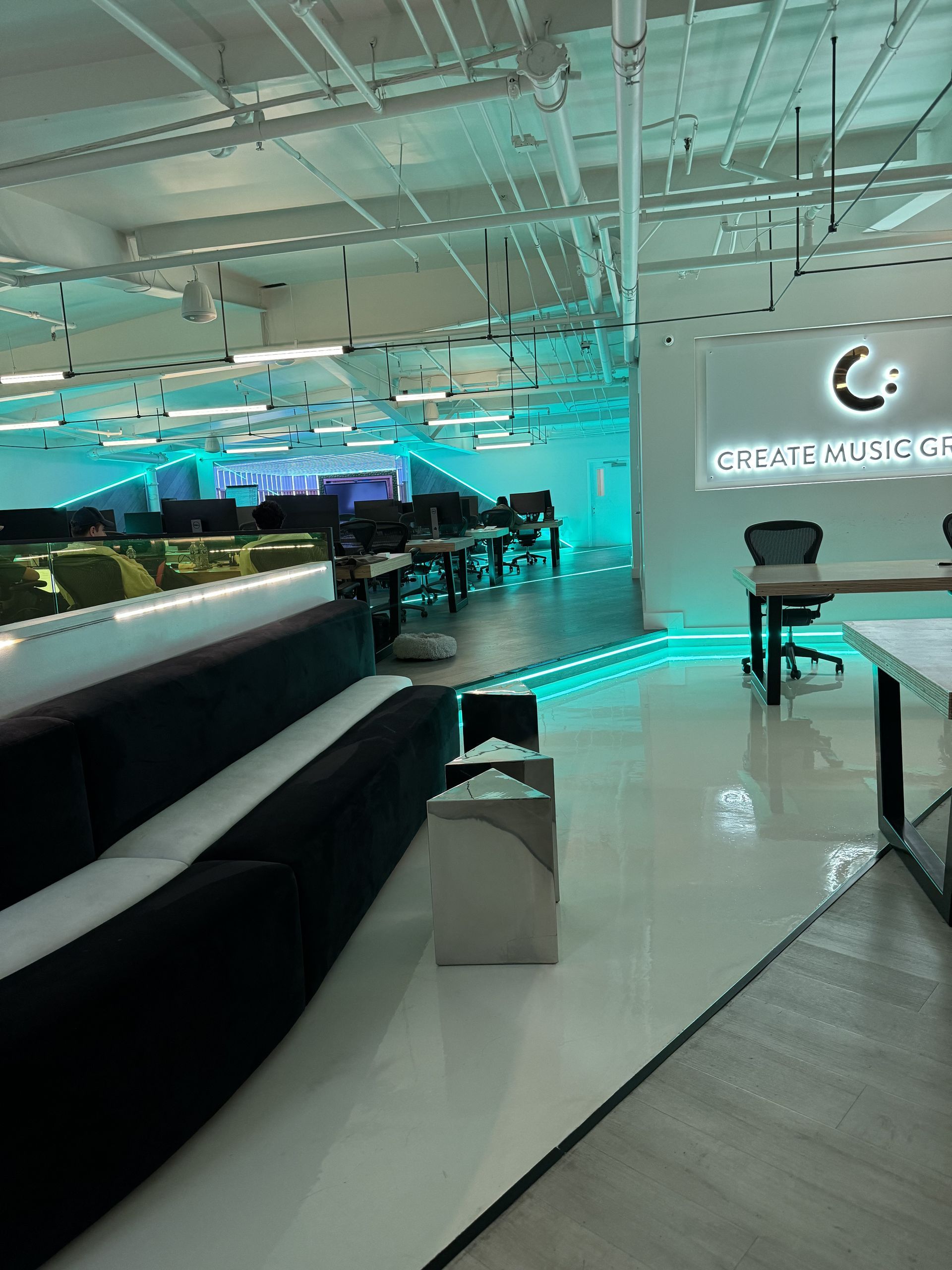 Modern office space with turquoise accents, seating, and desks. Sign reads 