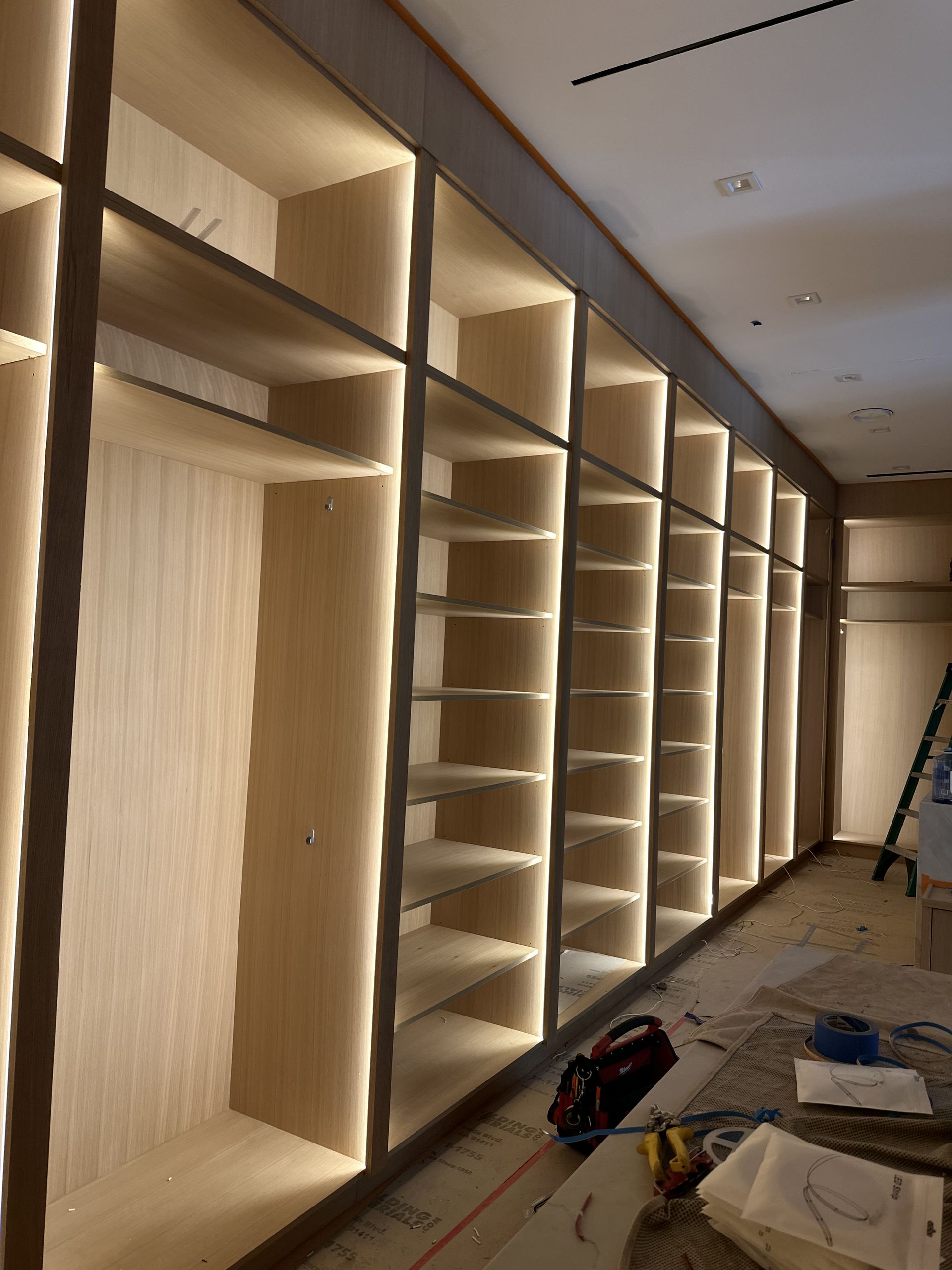 Built-in closet with interior lighting; wooden shelves and vertical dividers. Construction materials and tools visible.