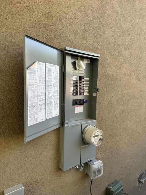 A electrical box with a meter attached to it is sitting on a wall.