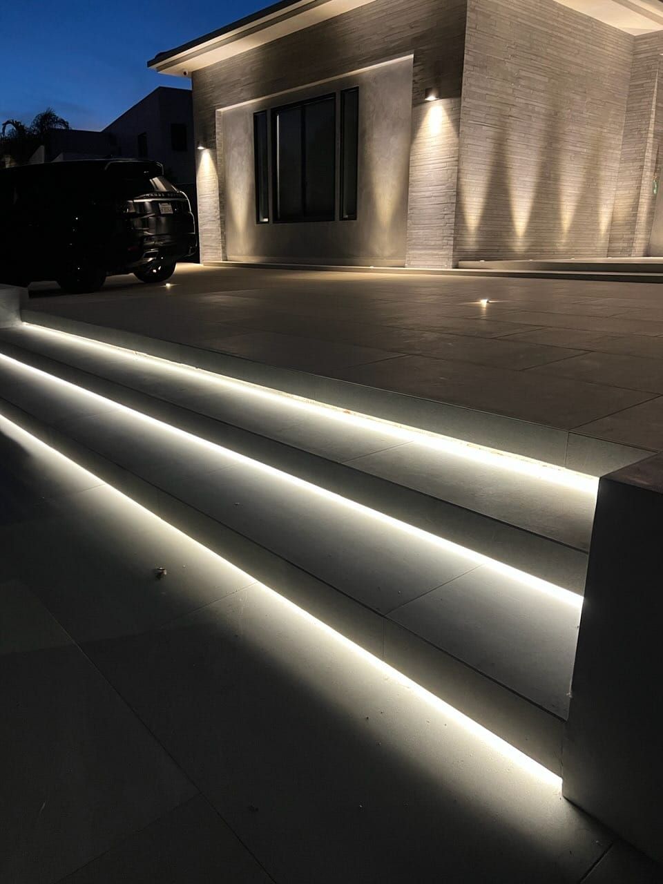 Exterior stairs with illuminated LED strips, leading to a modern house at night.