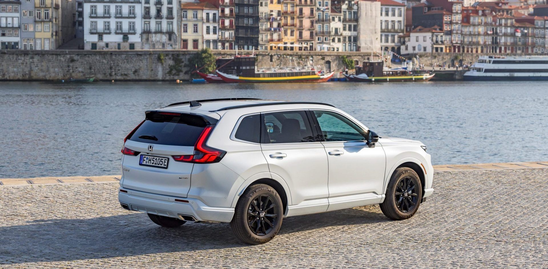 White SUV parked by a waterfront with city buildings in the background
