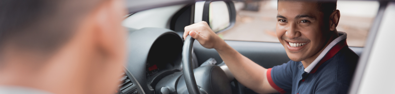 Um homem está sentado no banco do motorista de um carro e sorrindo.