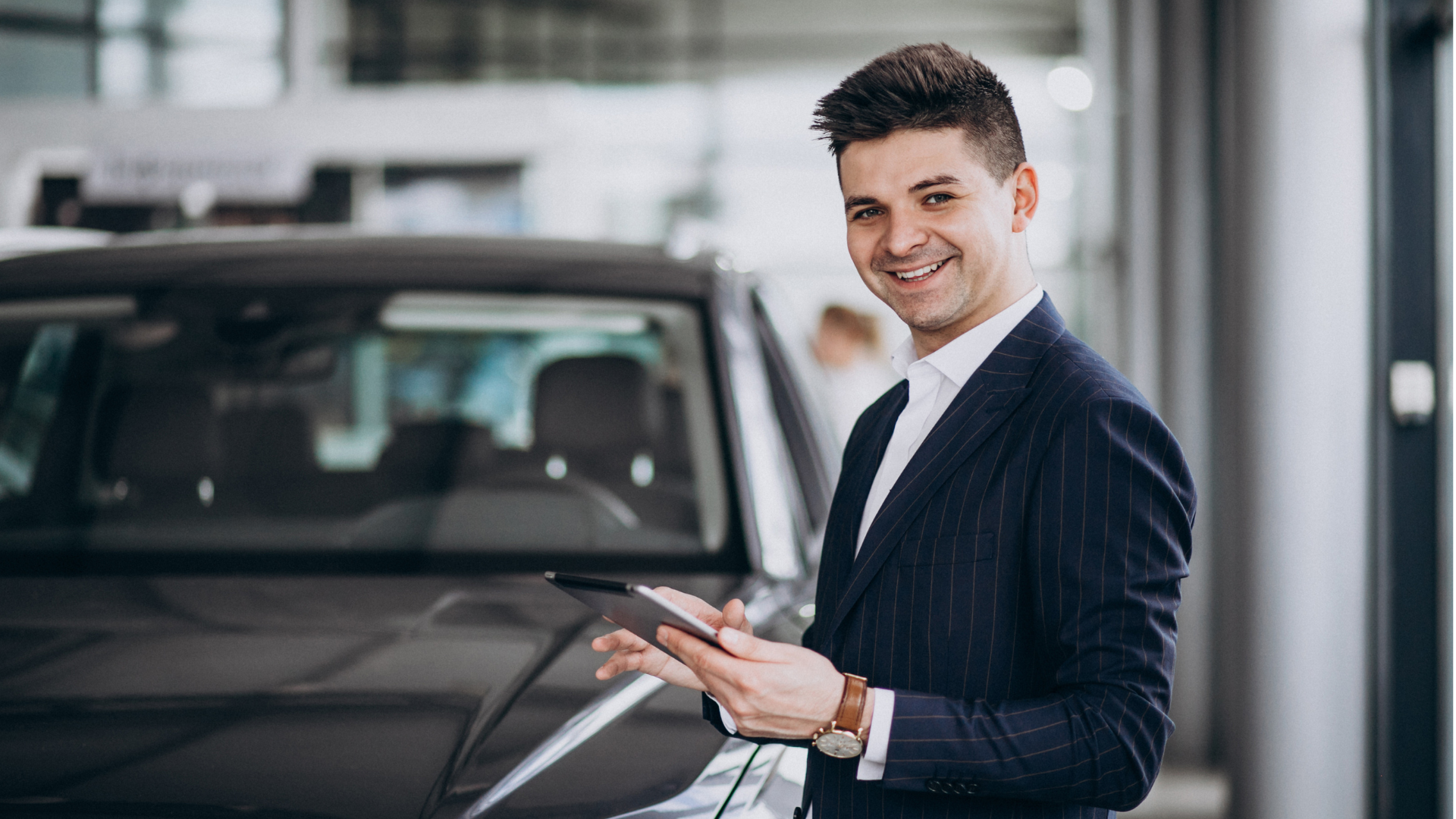 Um homem de terno está segurando um tablet na frente de um carro.