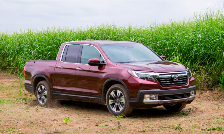 Uma picape honda ridgeline vermelha está estacionada em um campo de grama alta.