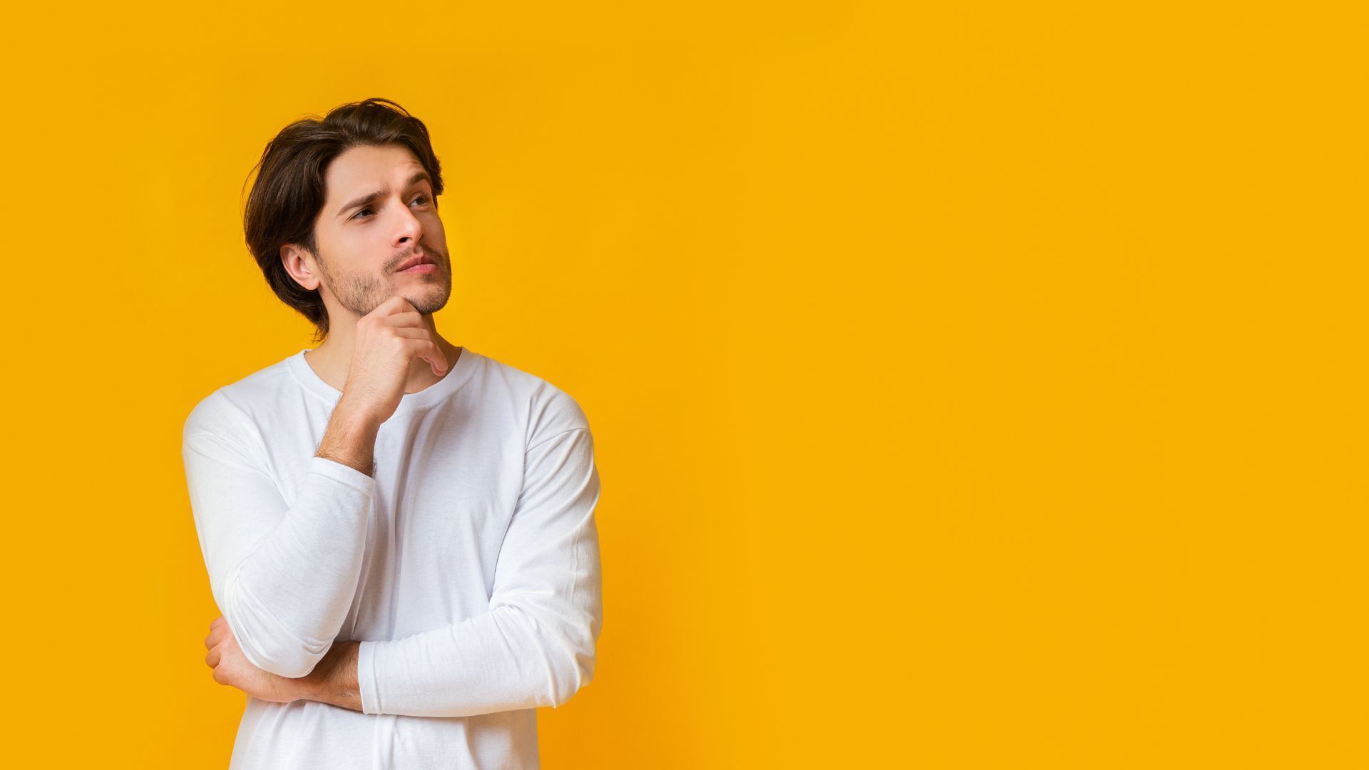 Man in white shirt resting chin on hand against a bright yellow background