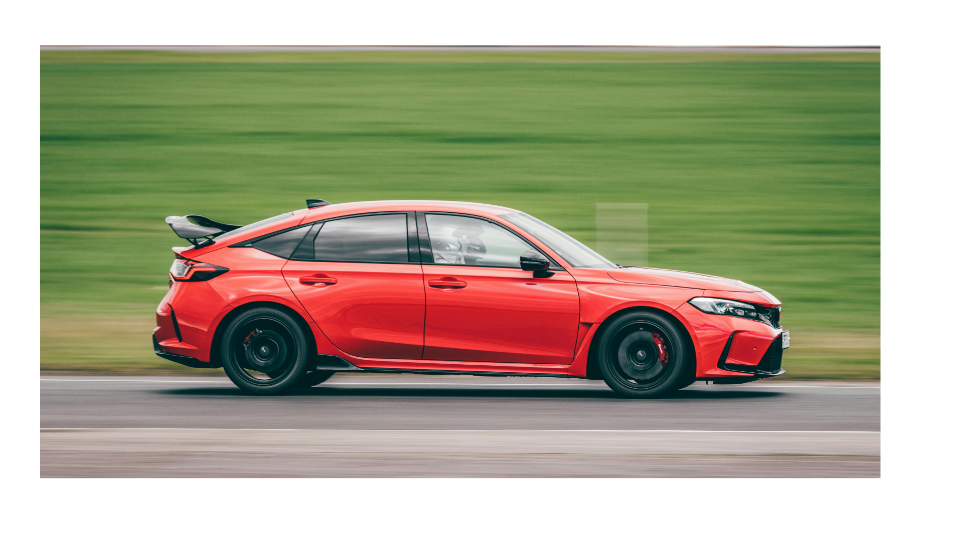 Red sports sedan driving fast on a road, side view against a blurred green background.