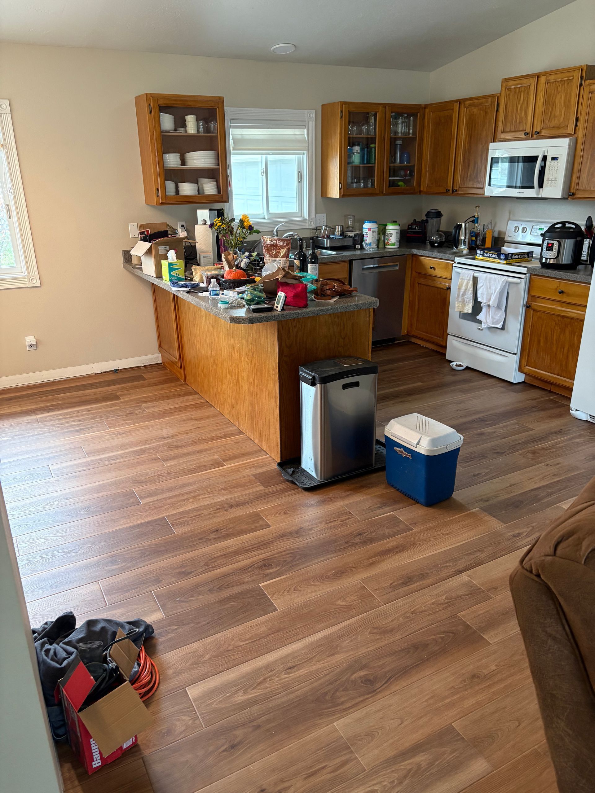 A kitchen with wooden cabinets , a stove , a microwave and a trash can.