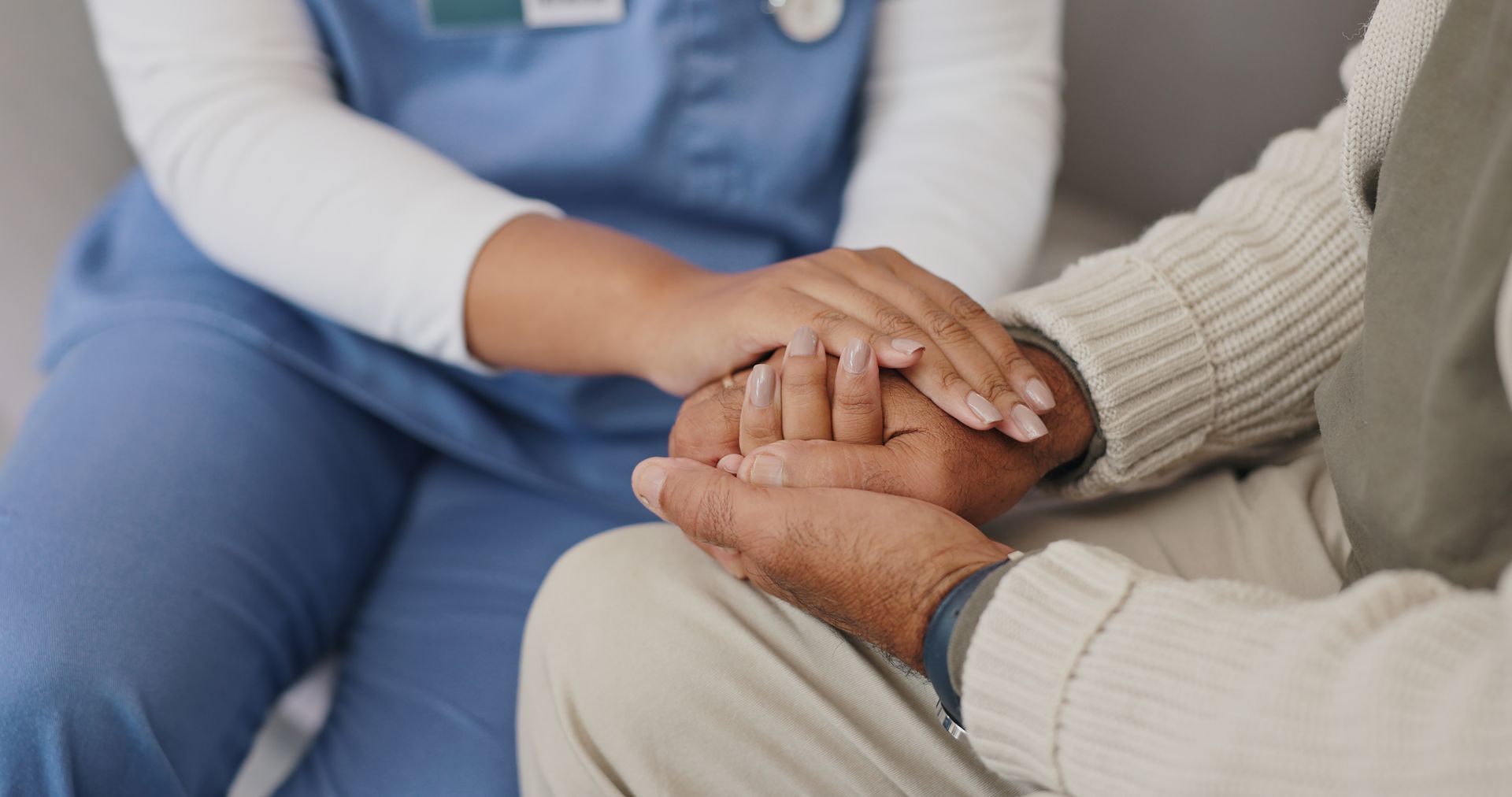 A nurse is holding the hand of an elderly man.