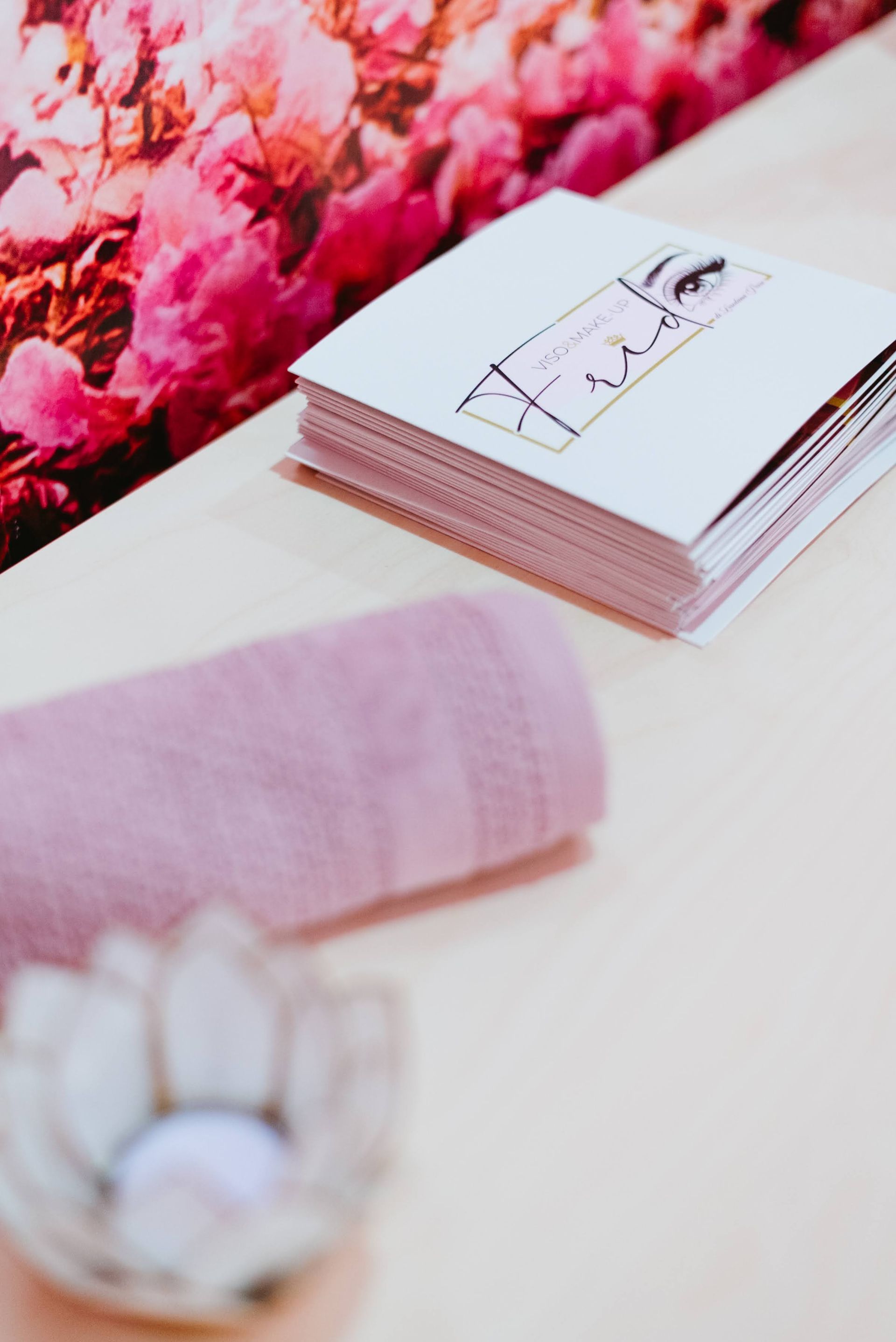 Asciugamano rosa, brochure e portacandele su una superficie di colore chiaro con uno sfondo floreale rosa.