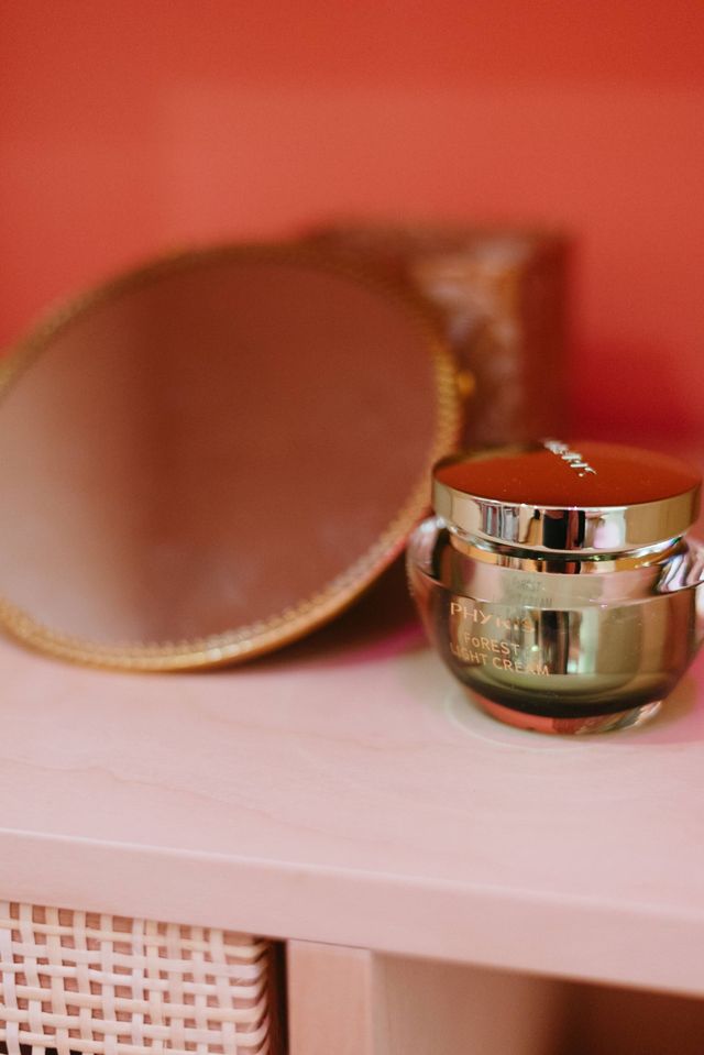 Barattolo di crema e specchio con bordo dorato su una mensola bianca su sfondo rosa.