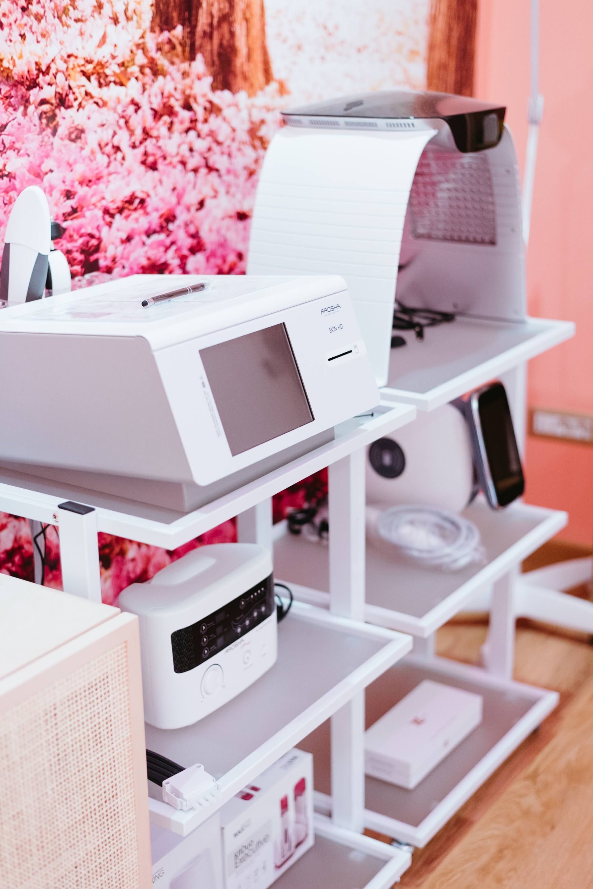 Attrezzature mediche bianche sugli scaffali, in una stanza con pareti rosa e decorazioni floreali.