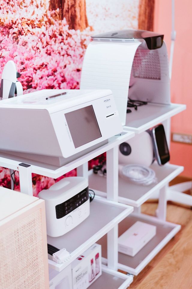 Attrezzature mediche bianche sugli scaffali, in una stanza con pareti rosa e decorazioni floreali.