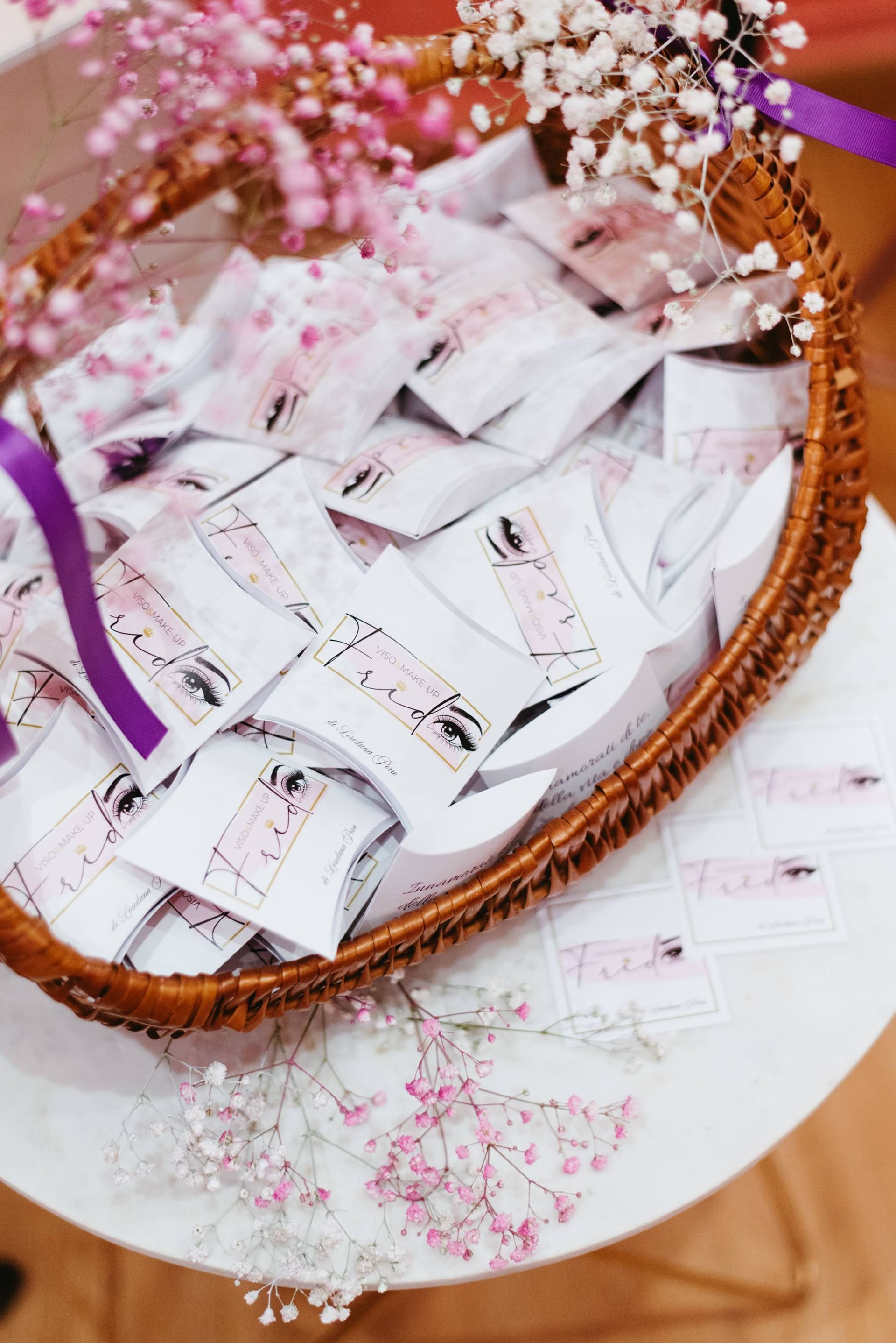 Cestino pieno di pacchetti bianchi, probabilmente bomboniere, decorato con fiori e un nastro viola.