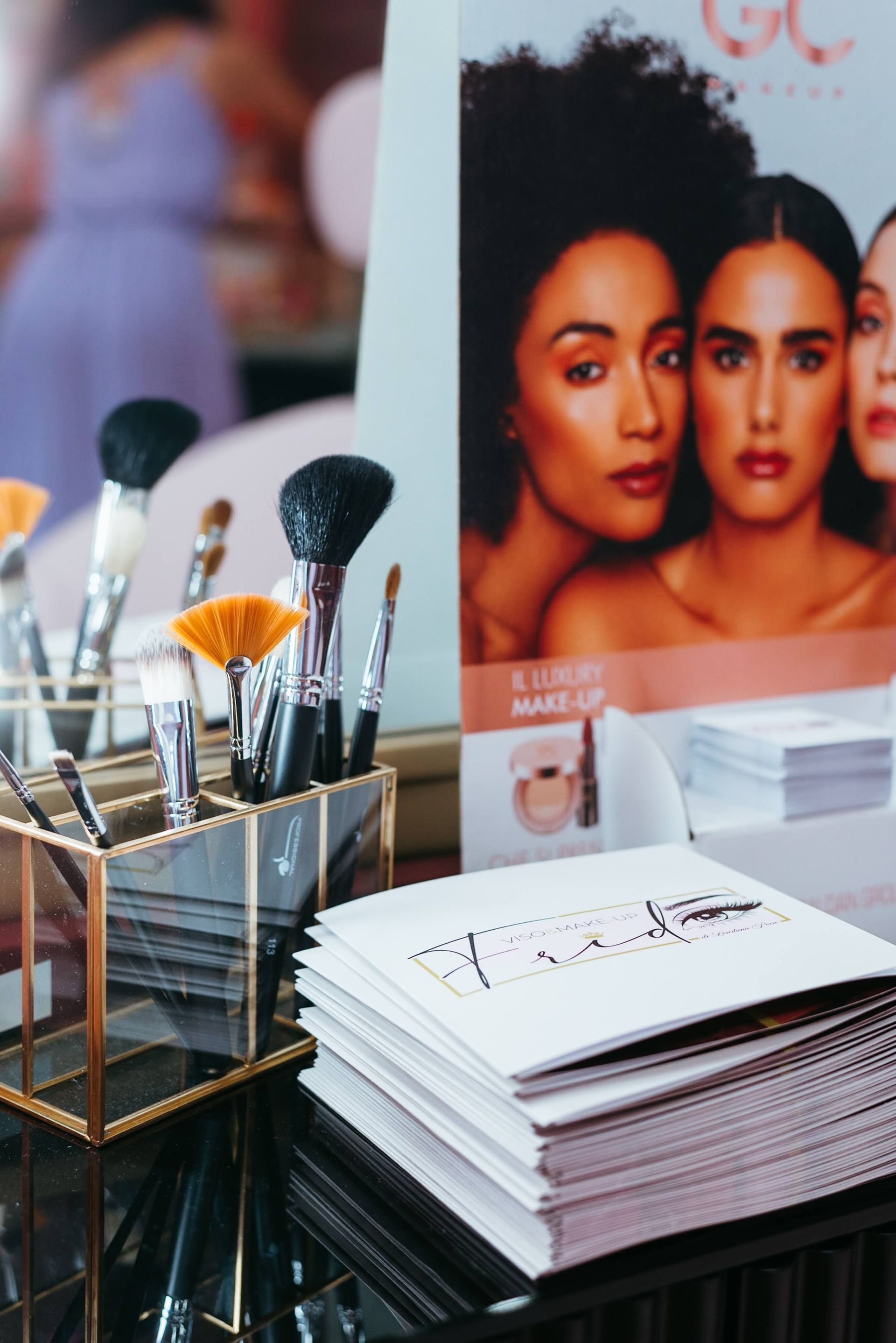 Pennelli per il trucco e brochure sul tavolo vicino a un espositore promozionale raffigurante volti di donne.