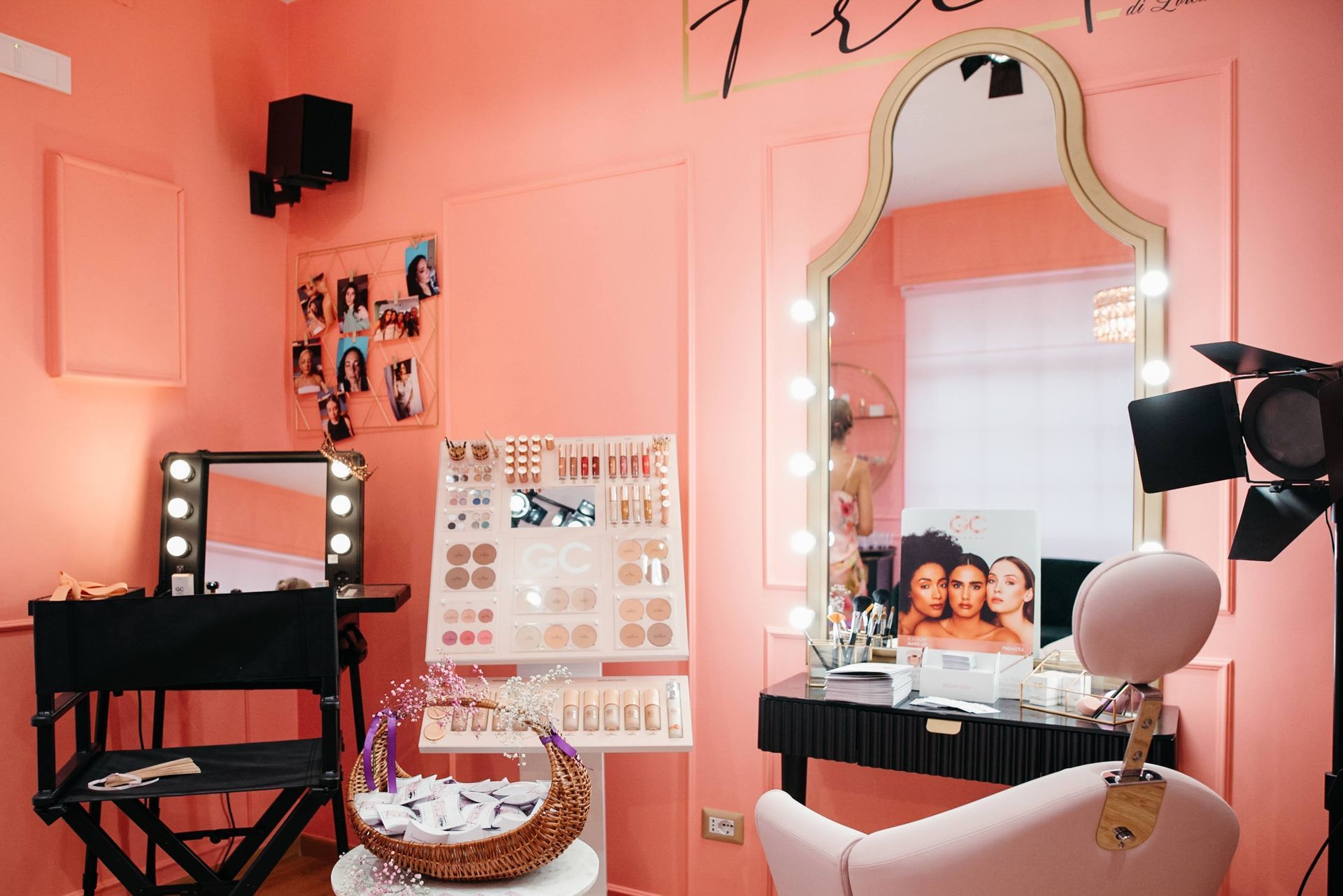 Studio di trucco rosa con specchio, prodotti e illuminazione.