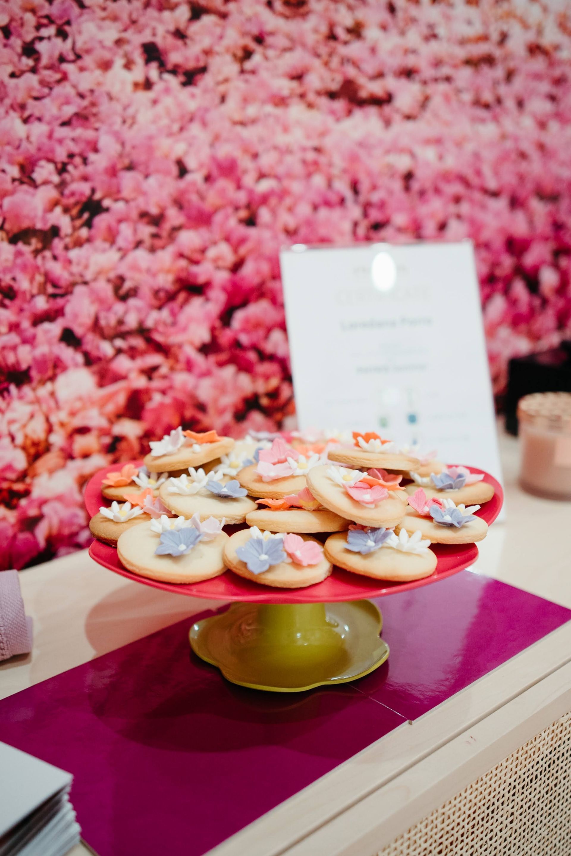 Biscotti con glassa floreale su un'alzata per torte rossa, su uno sfondo floreale rosa.