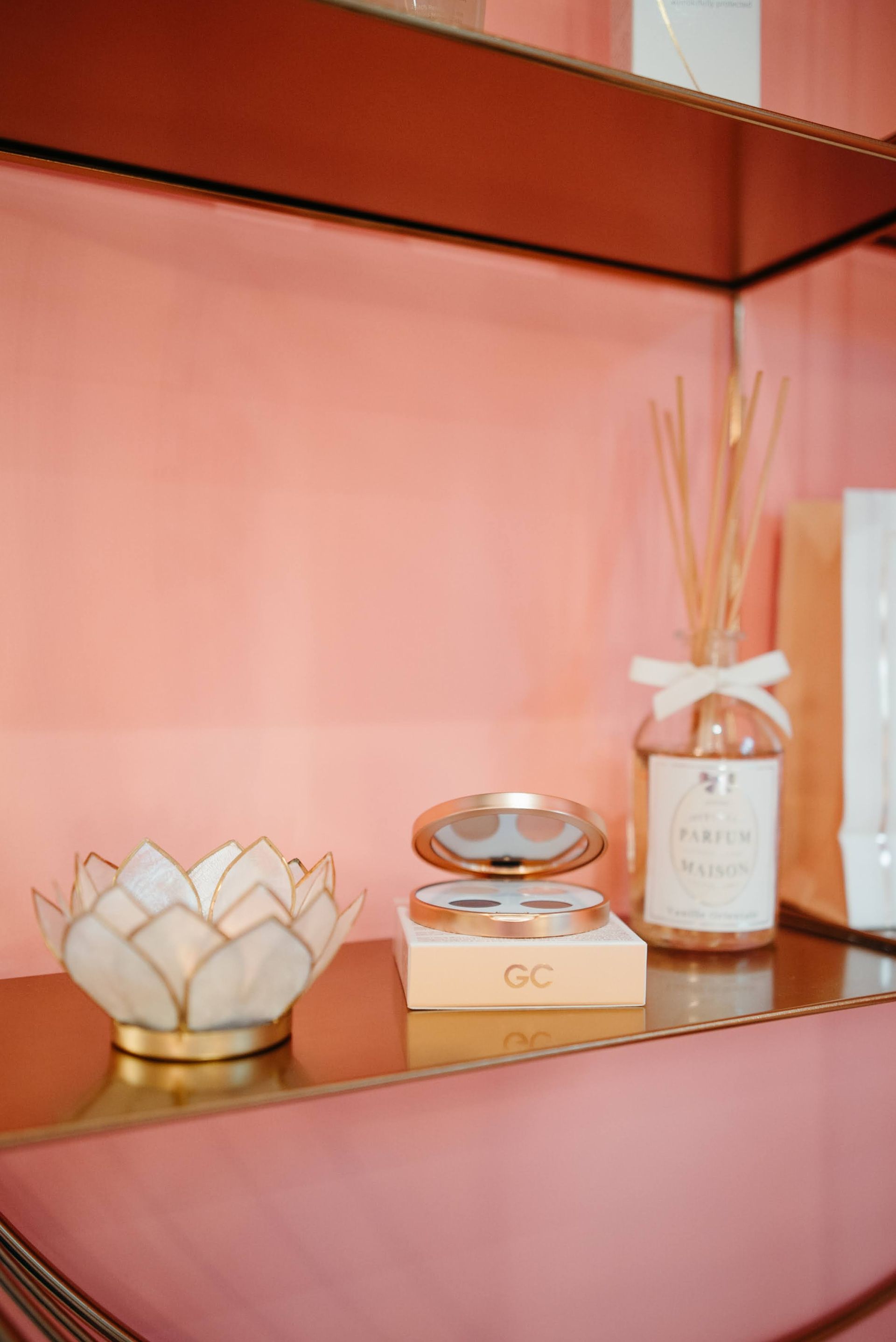 Mensola rosa con portacandele decorativo a forma di fiore di loto, flacone compatto aperto e diffusore a bastoncini.