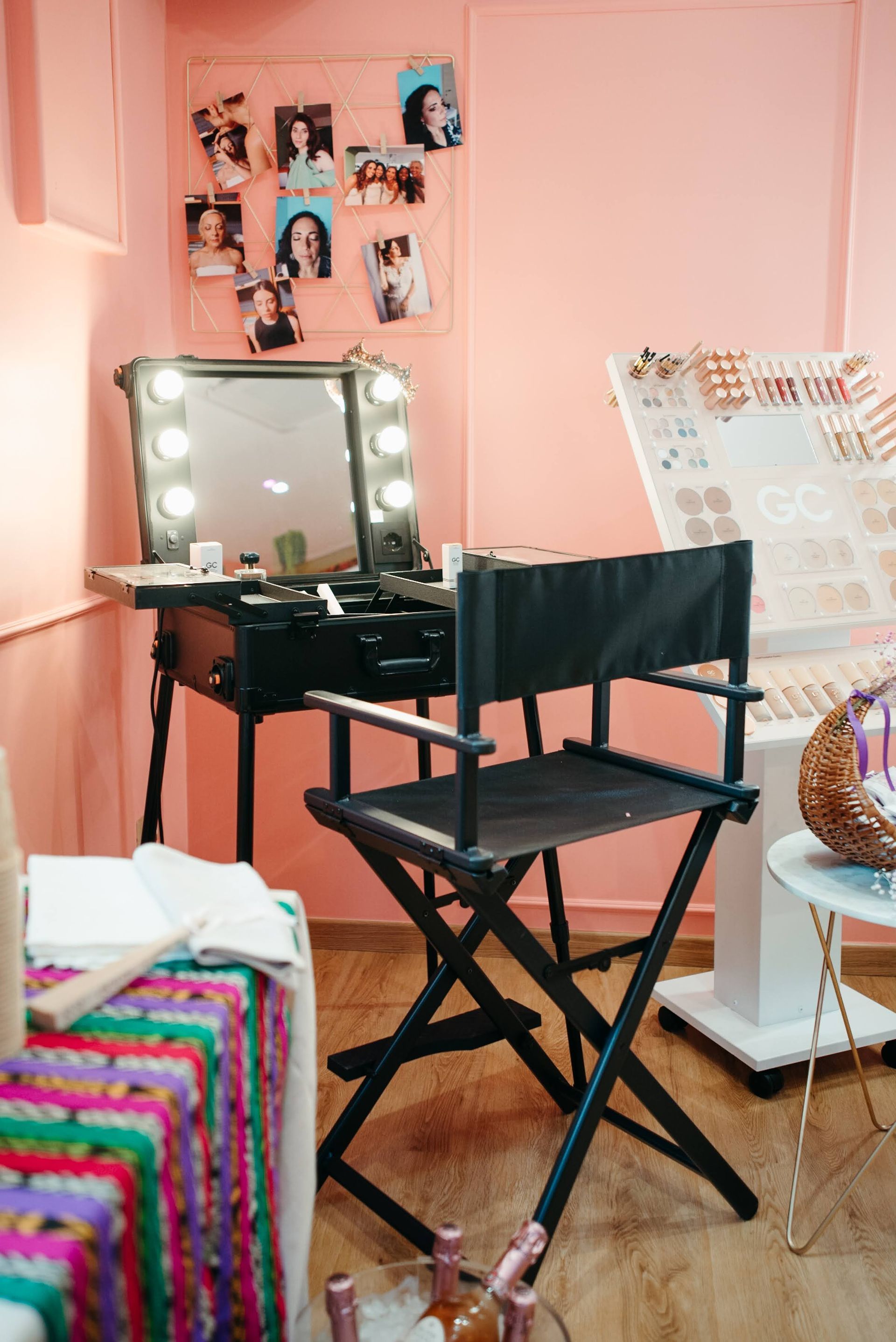 Postazione trucco con sedia da regista in una stanza dalle pareti rosa, dotata di specchio illuminato, cosmetici e espositore per gioielli.