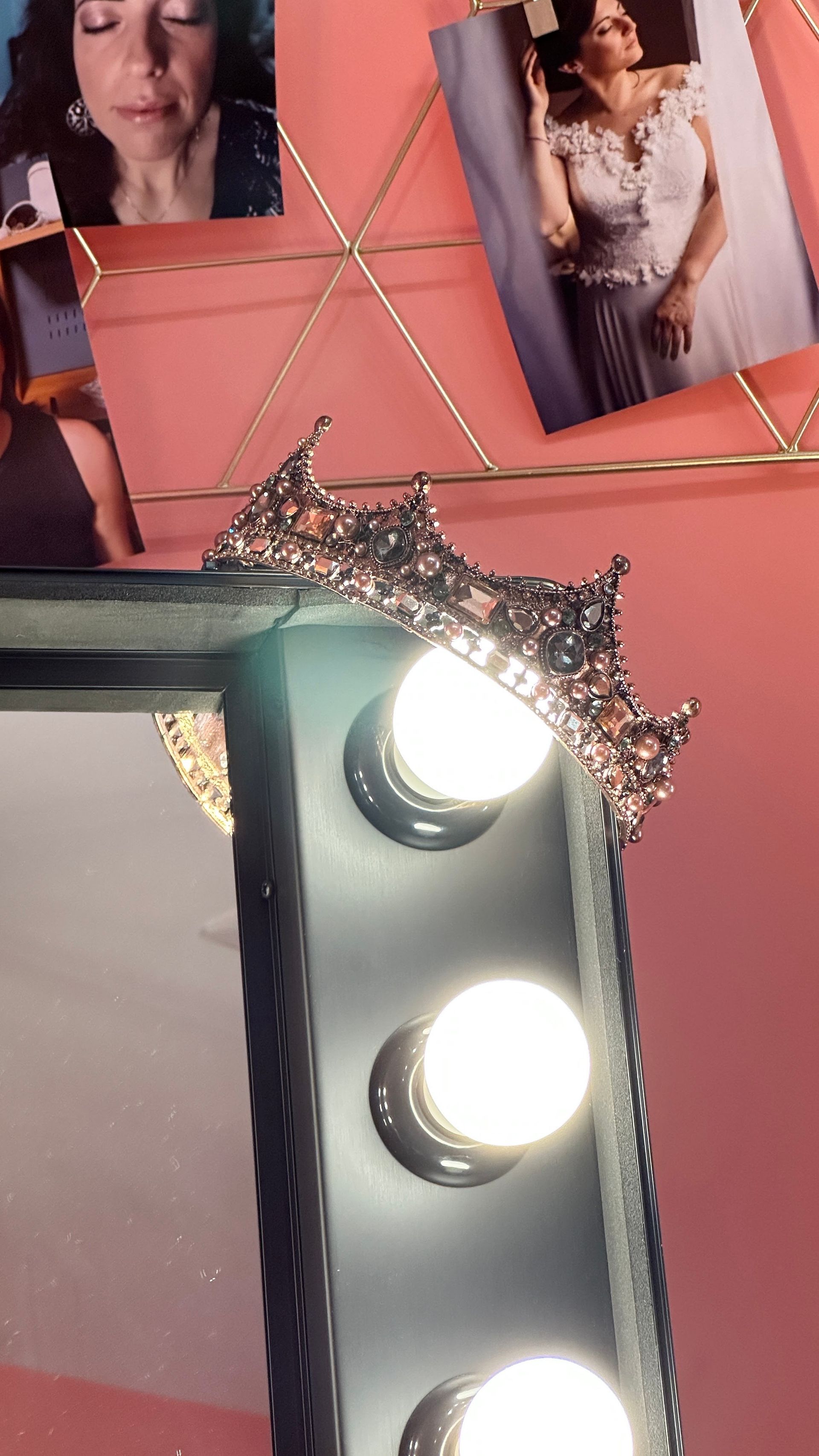 Corona sullo specchio da toeletta con luci; foto sullo sfondo. Sfondo rosa.