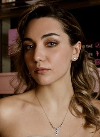 Donna dalla pelle chiara, con indosso una collana. Ha i capelli castano chiaro e guarda in camera.