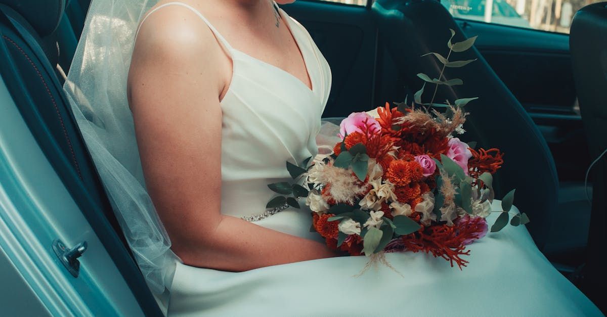 A bride is sitting in the back seat of a car holding a bouquet of flowers.