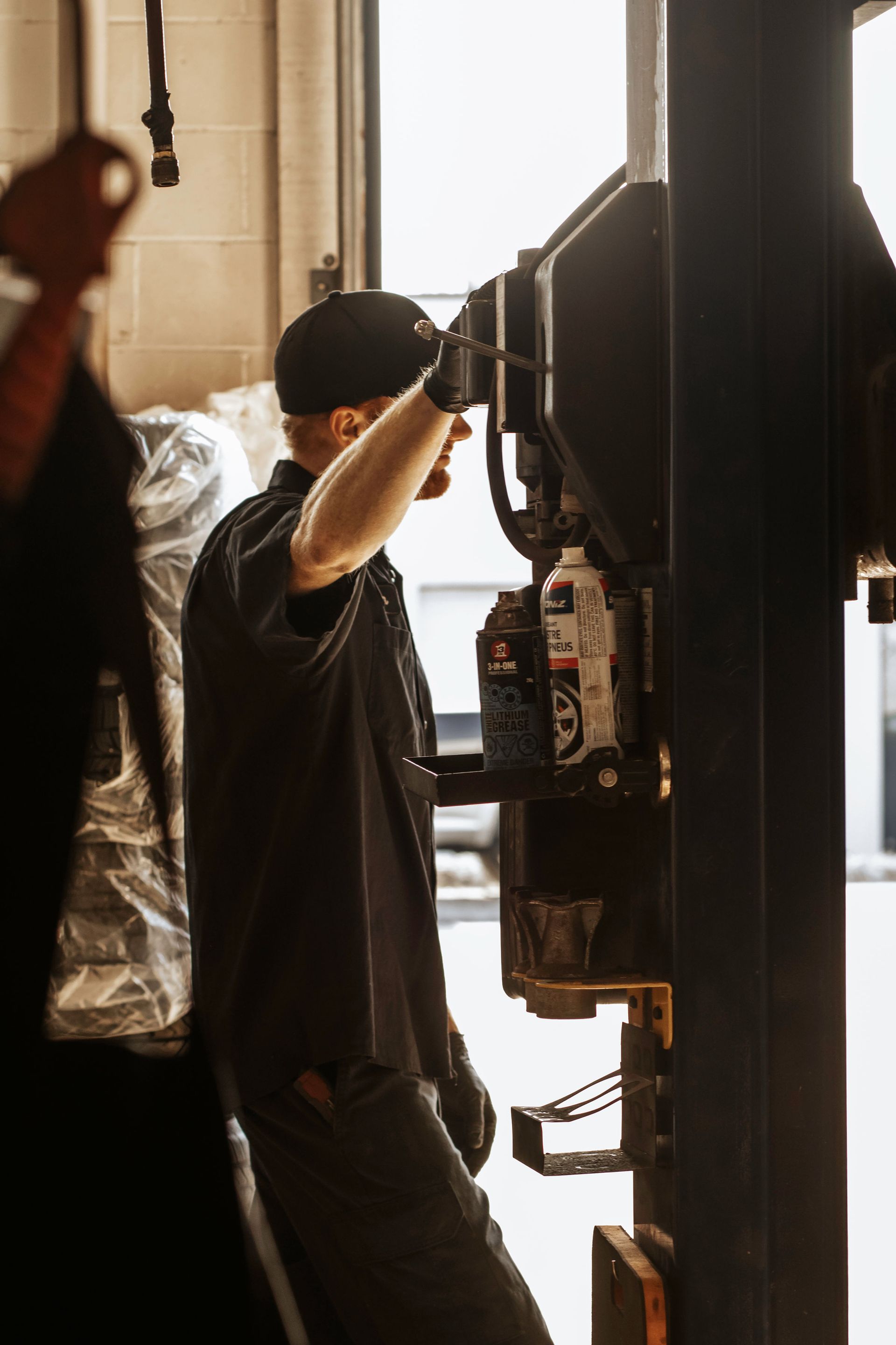 Mechanic in black uniform adjusts machinery in a garage.