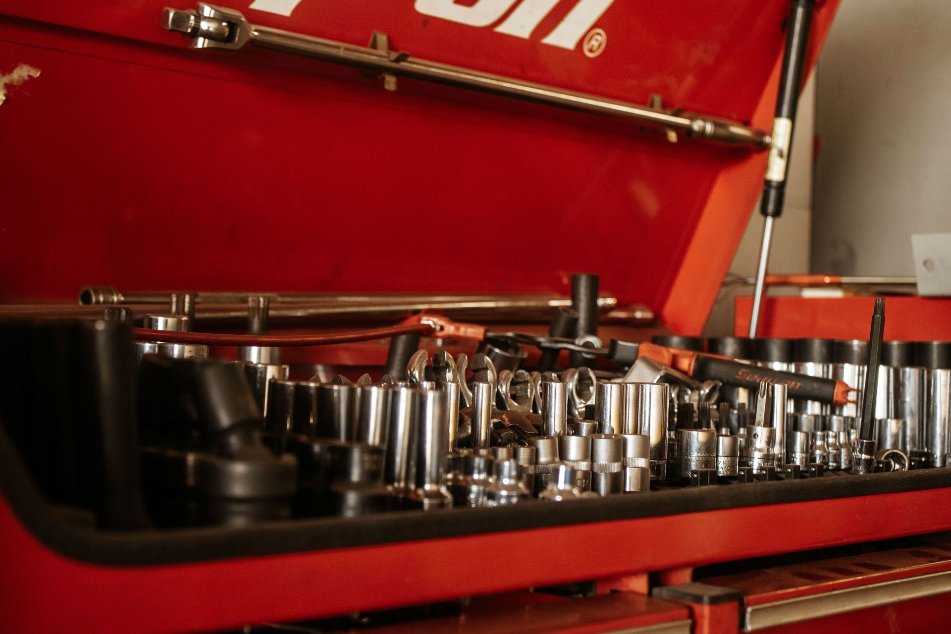 Red toolbox open, filled with various silver sockets, wrenches, and tools.