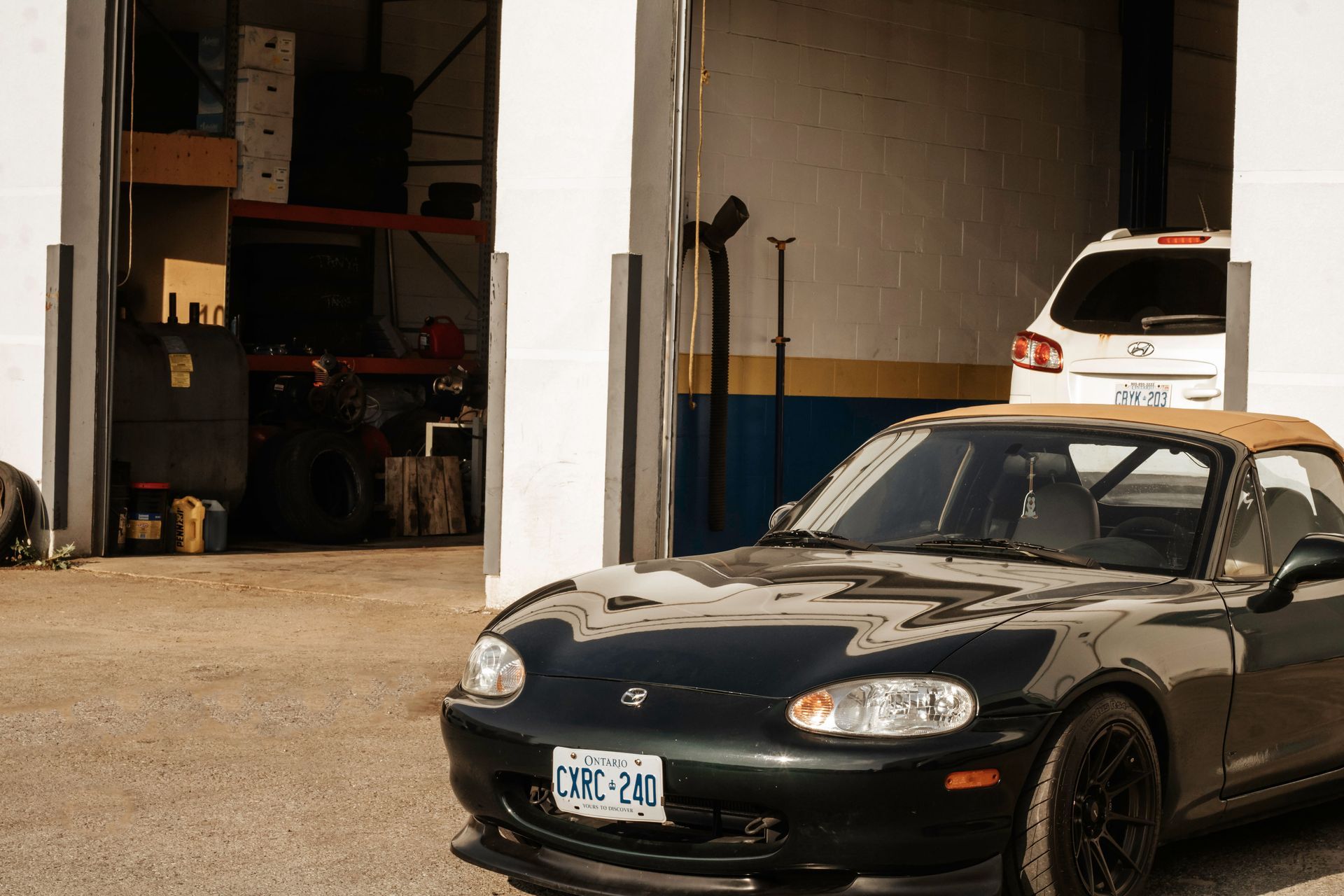 Dark green Mazda Miata convertible parked in front of a garage.