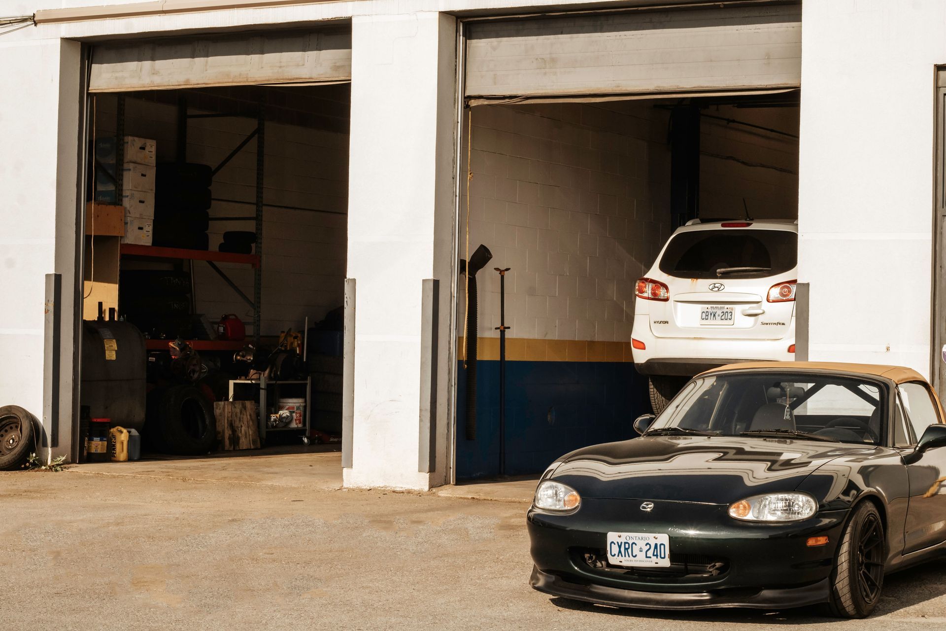 Black sports car outside a garage with a white SUV on a lift inside.