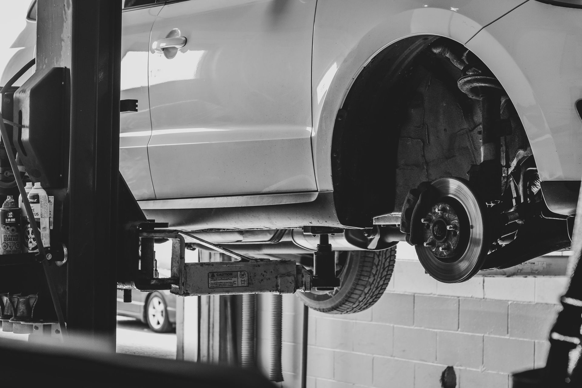 Car on a lift in a garage, wheel removed, showing brake components.