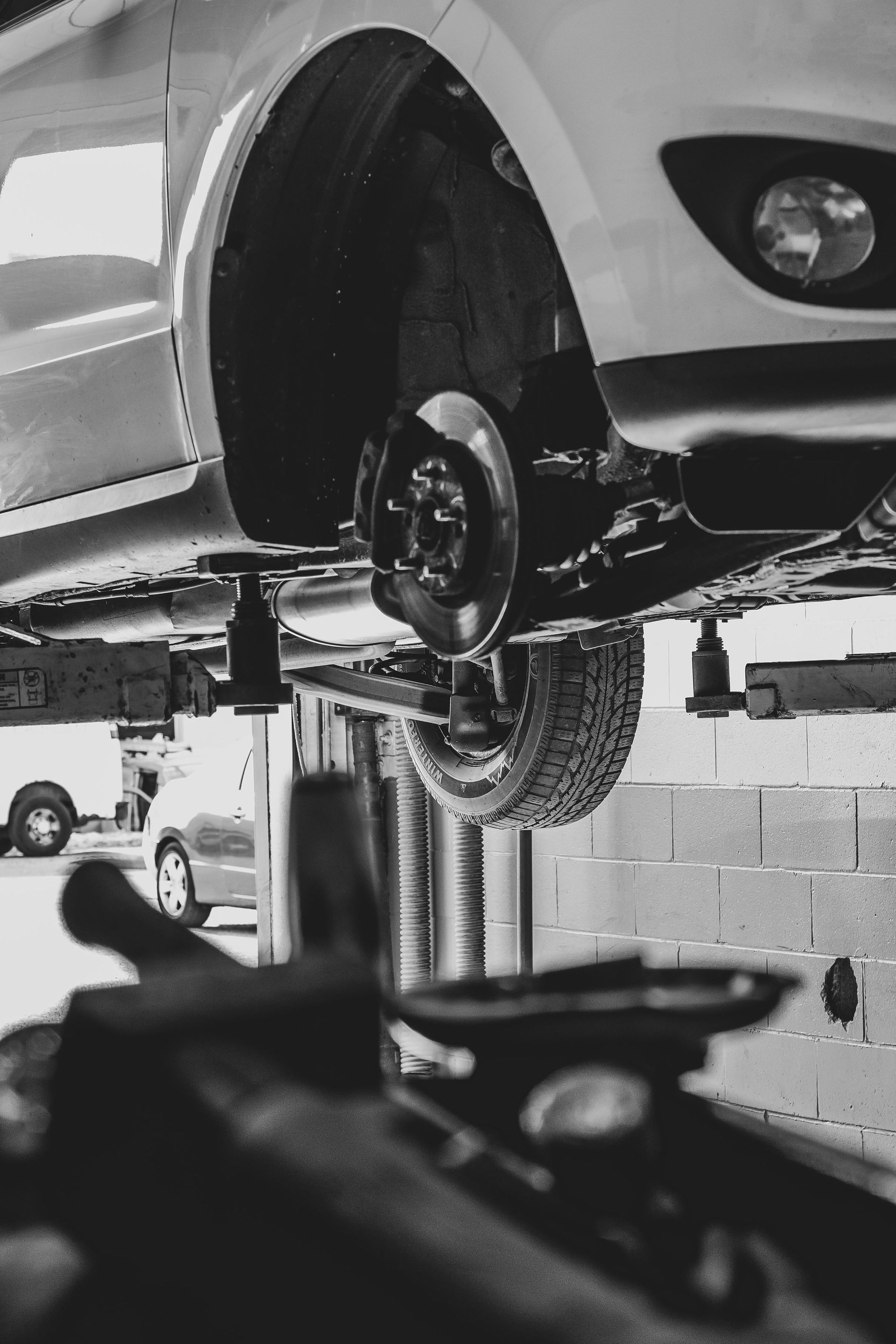 Car raised on a lift in a garage, wheel removed, exposing the brakes.