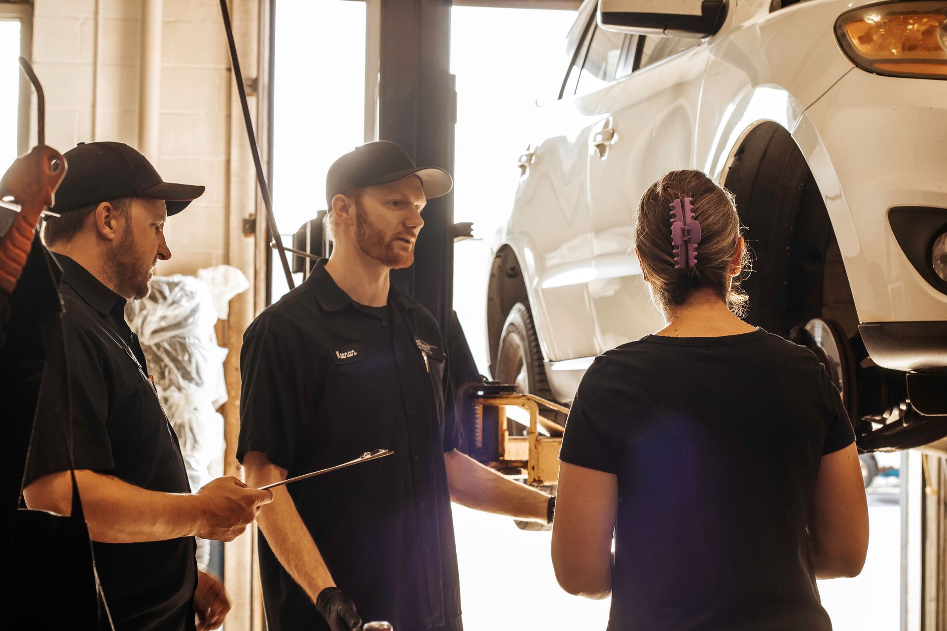 Mechanic explaining car repair to customer, two other mechanics nearby.