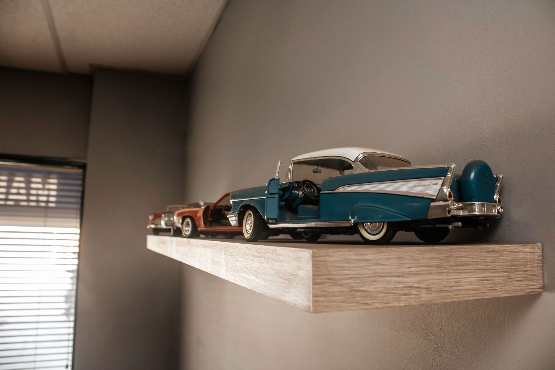 Two classic model cars on a light wood shelf against a gray wall.