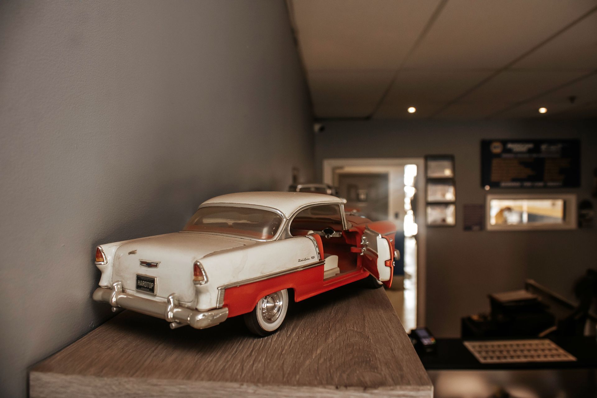 Toy classic red and white car on a wooden surface, next to a gray wall, door and interior in background.
