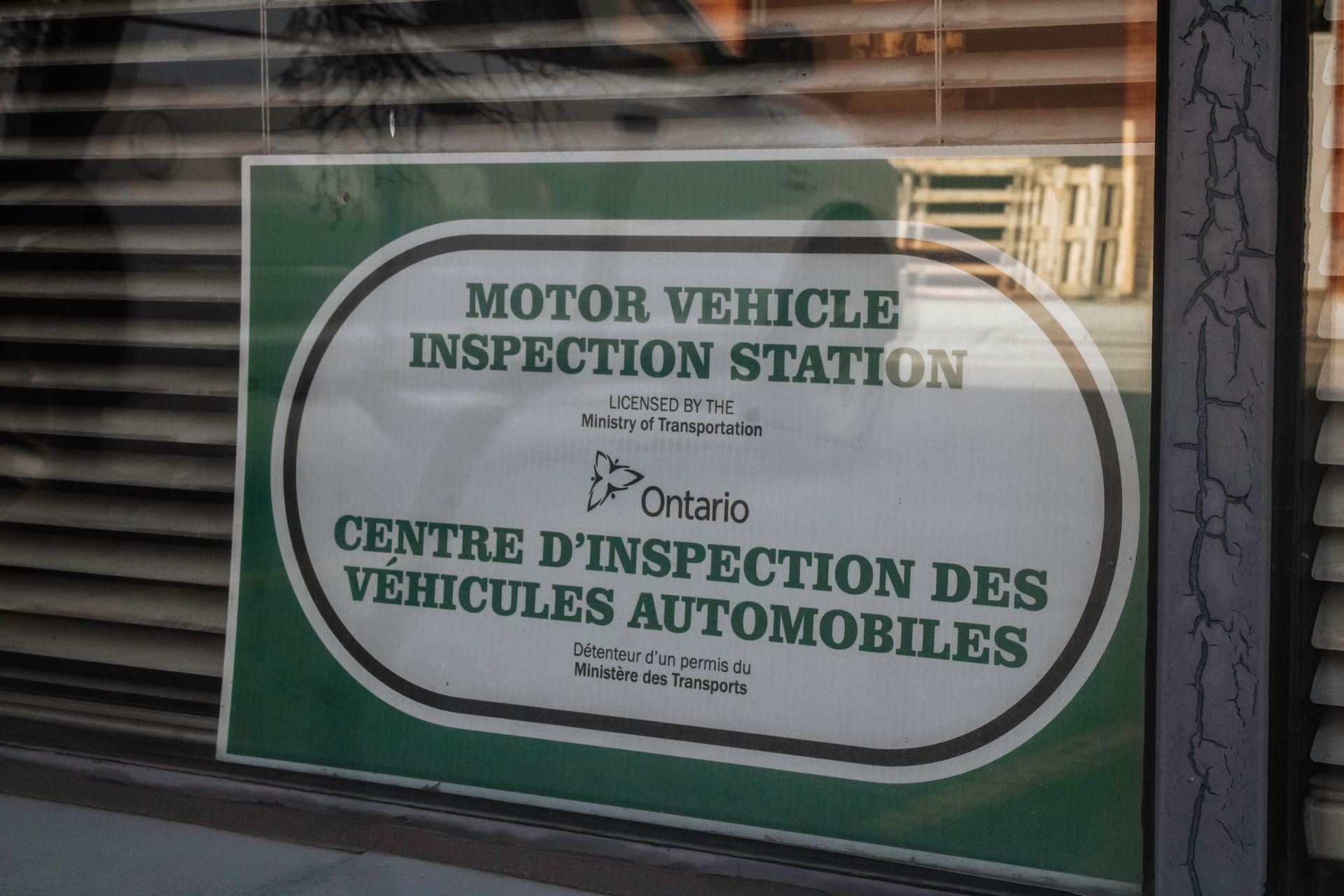Sign for a motor vehicle inspection station in Ontario, with text in English and French, in a window.