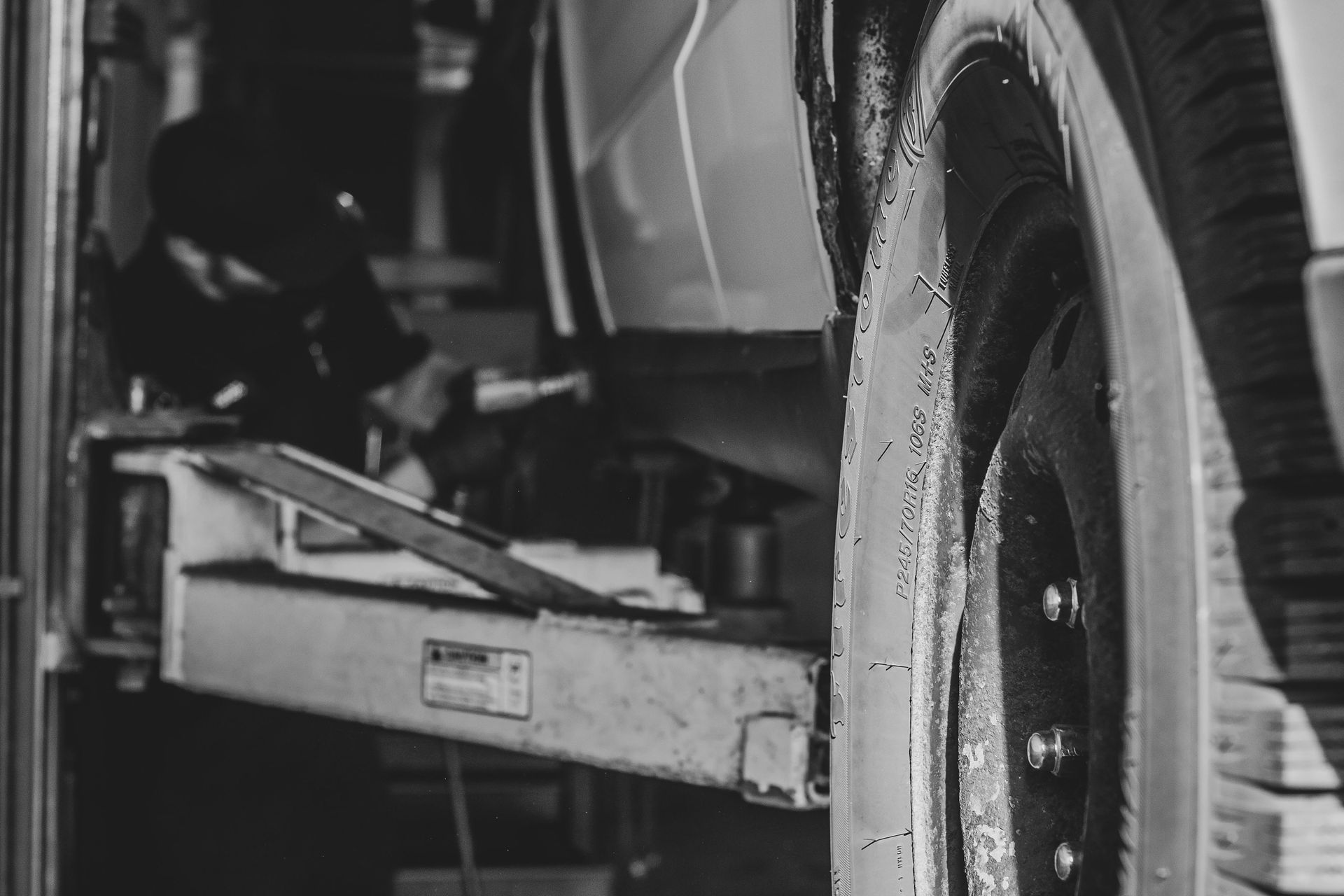 Car on a lift in a mechanic shop, wheel in focus.
