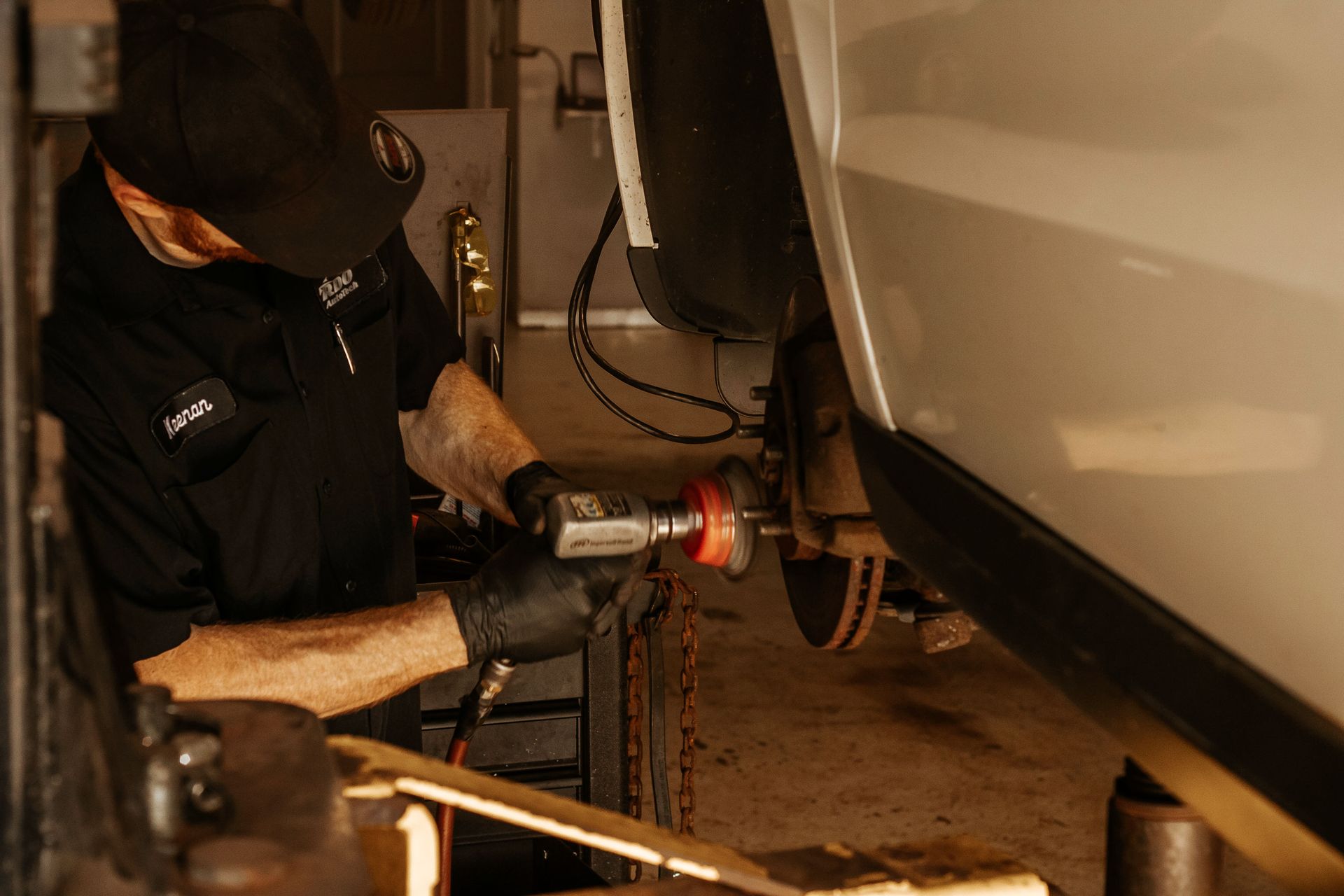 Mechanic using a tool on a vehicle's brake rotor in a garage.