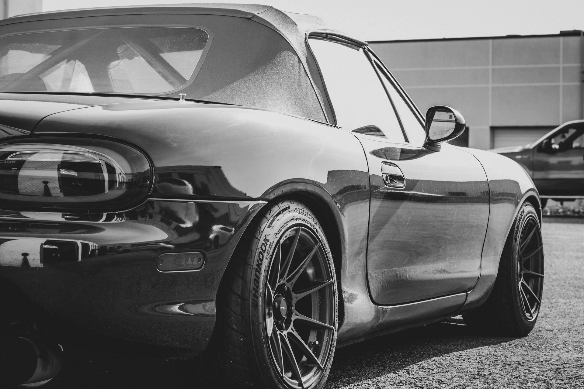 Black Miata sports car with custom wheels parked outside.