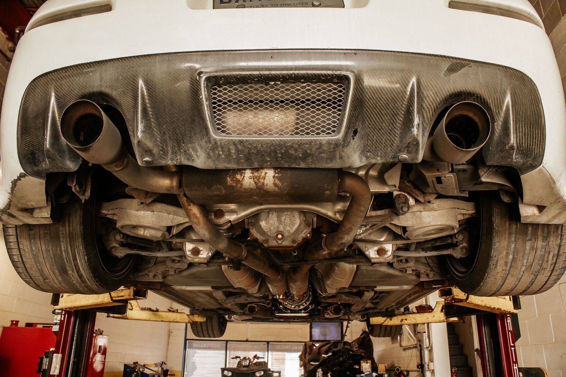 Undercarriage of a white sports car on a lift, showing exhaust system and rear diffuser.