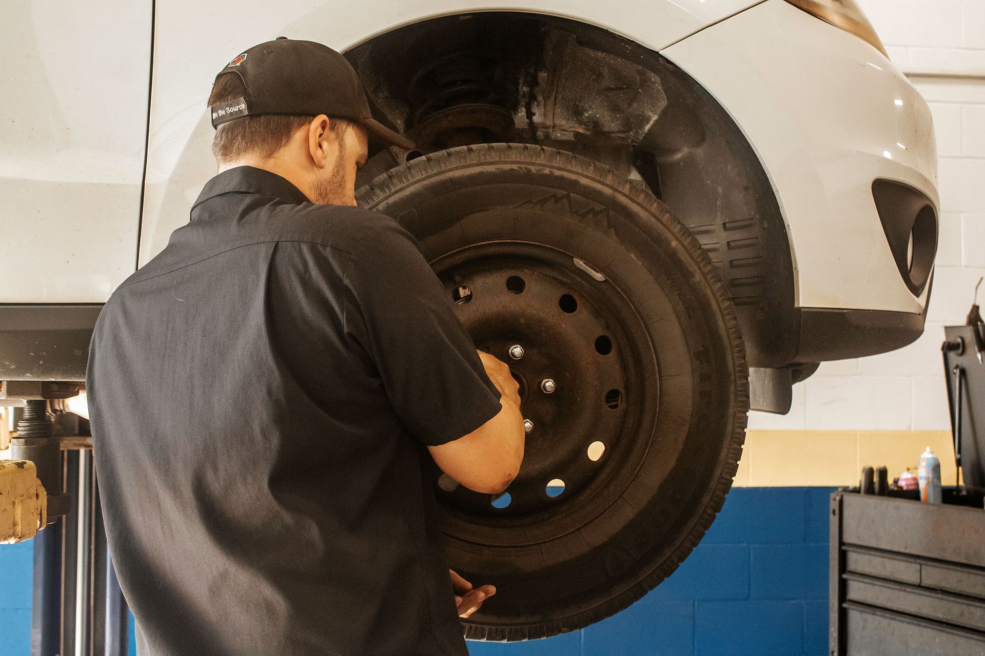 Mechanic removing a tire from a car on a lift in a shop.